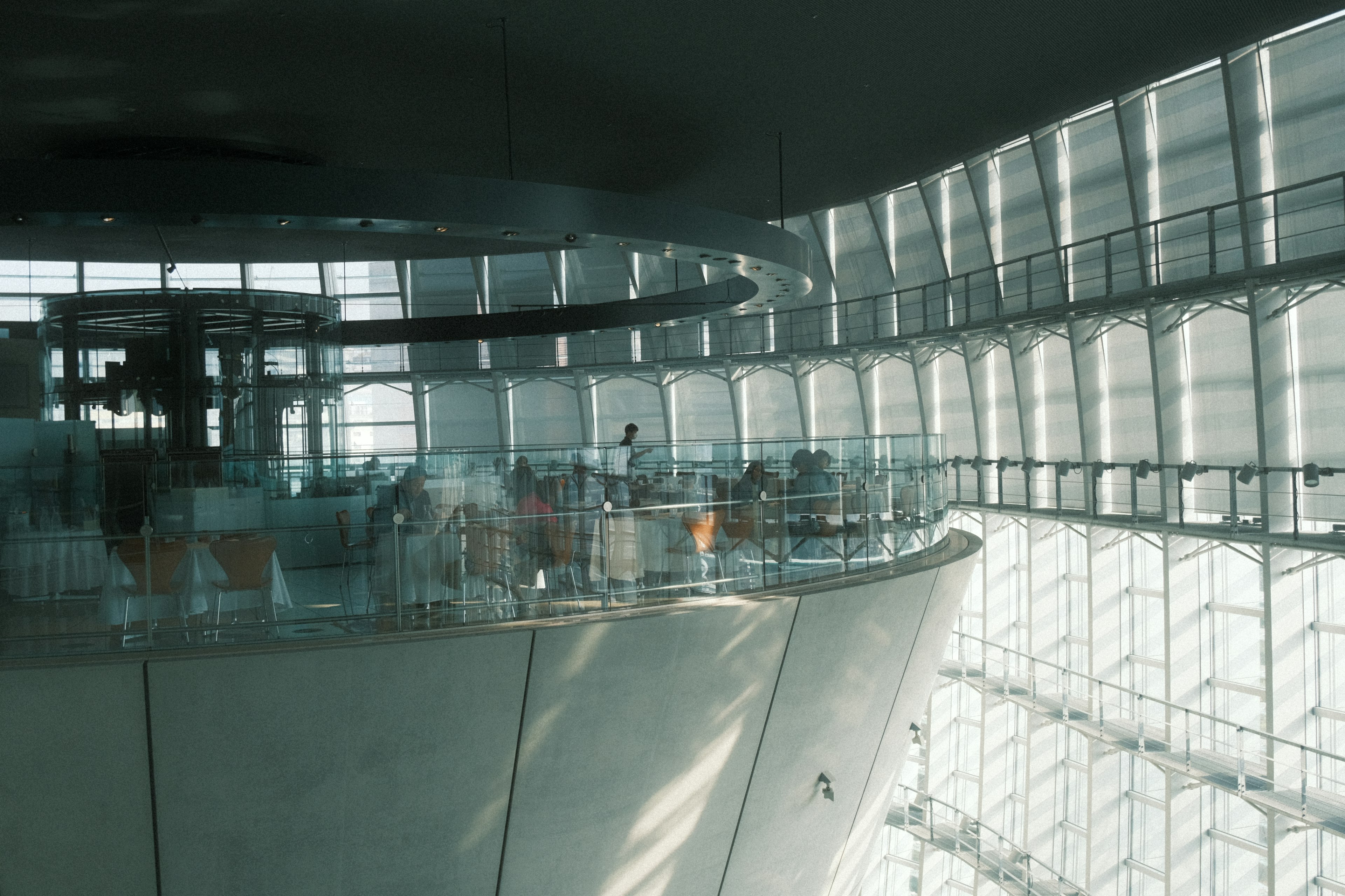 Interior de un espacio arquitectónico moderno con grandes ventanales y un balcón curvo iluminado por luz natural