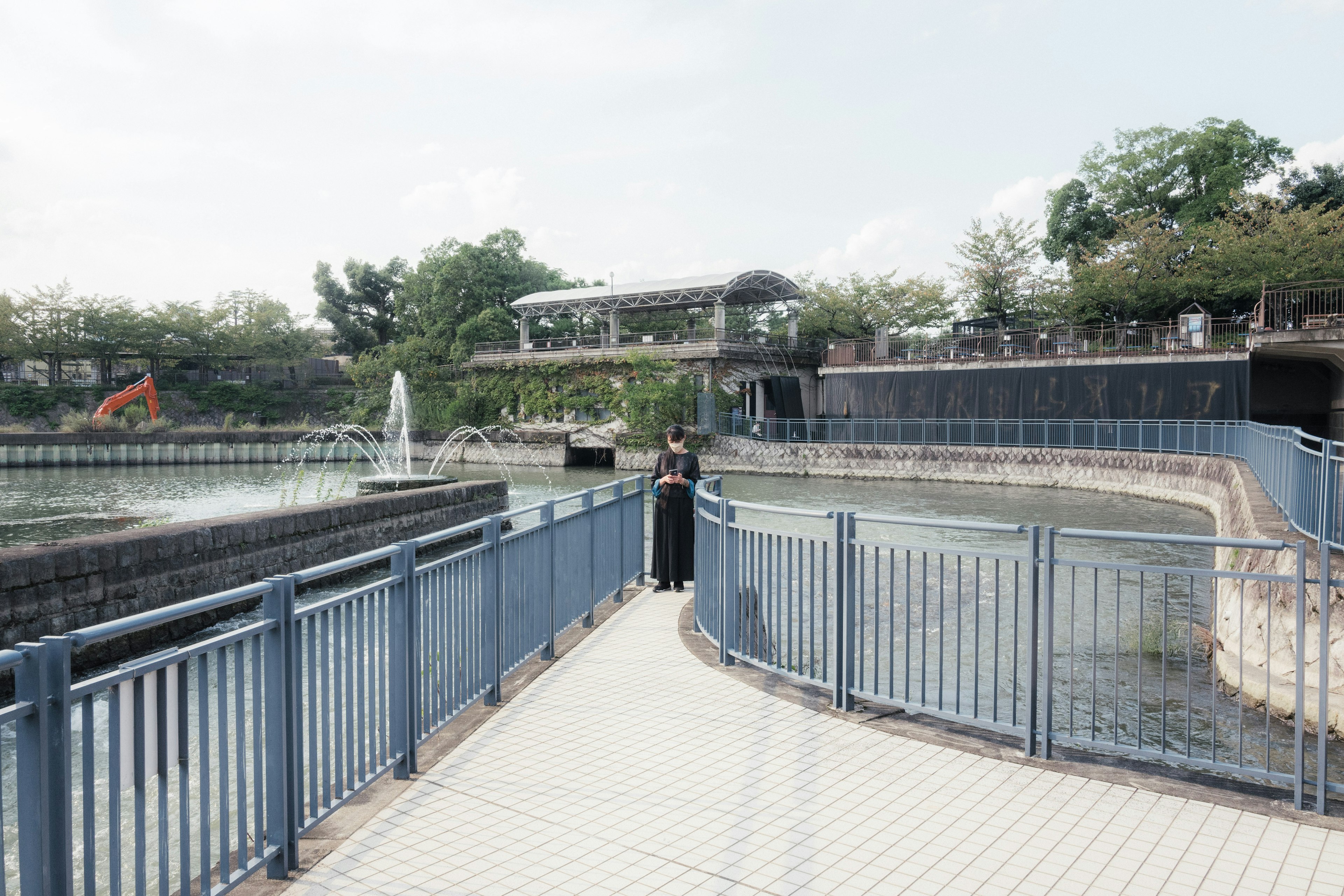 公園の水辺に立つ人物と青い手すりの歩道