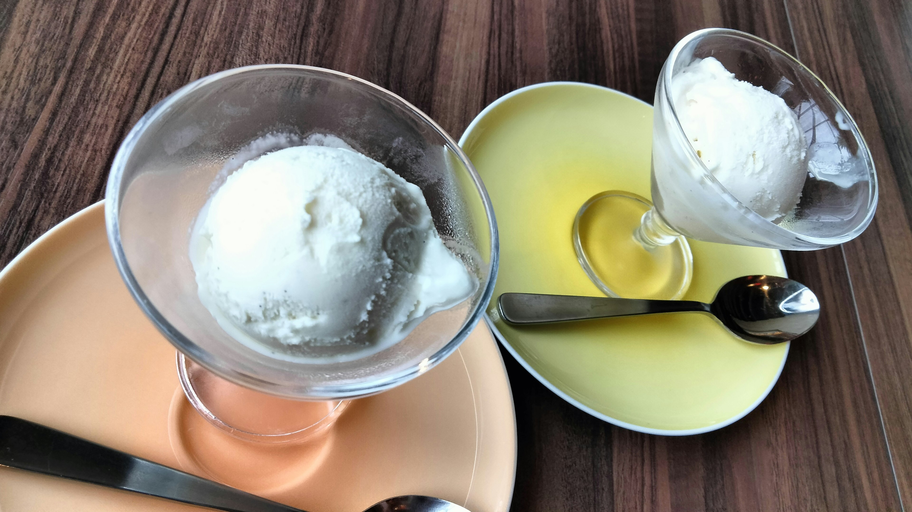 Two bowls of ice cream on different colored plates with silver spoons