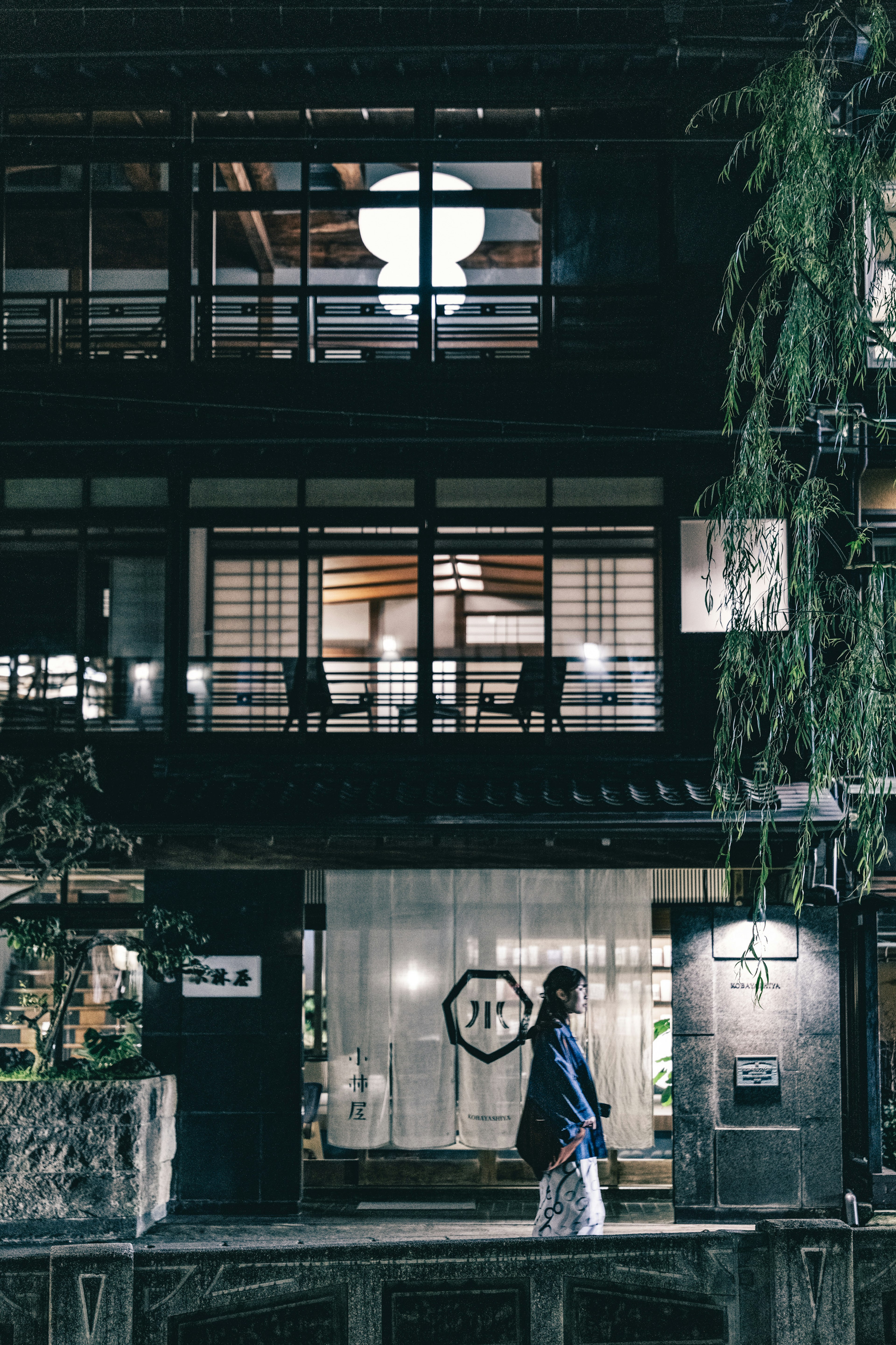 夜の街並みの古い日本家屋とその前を歩く人