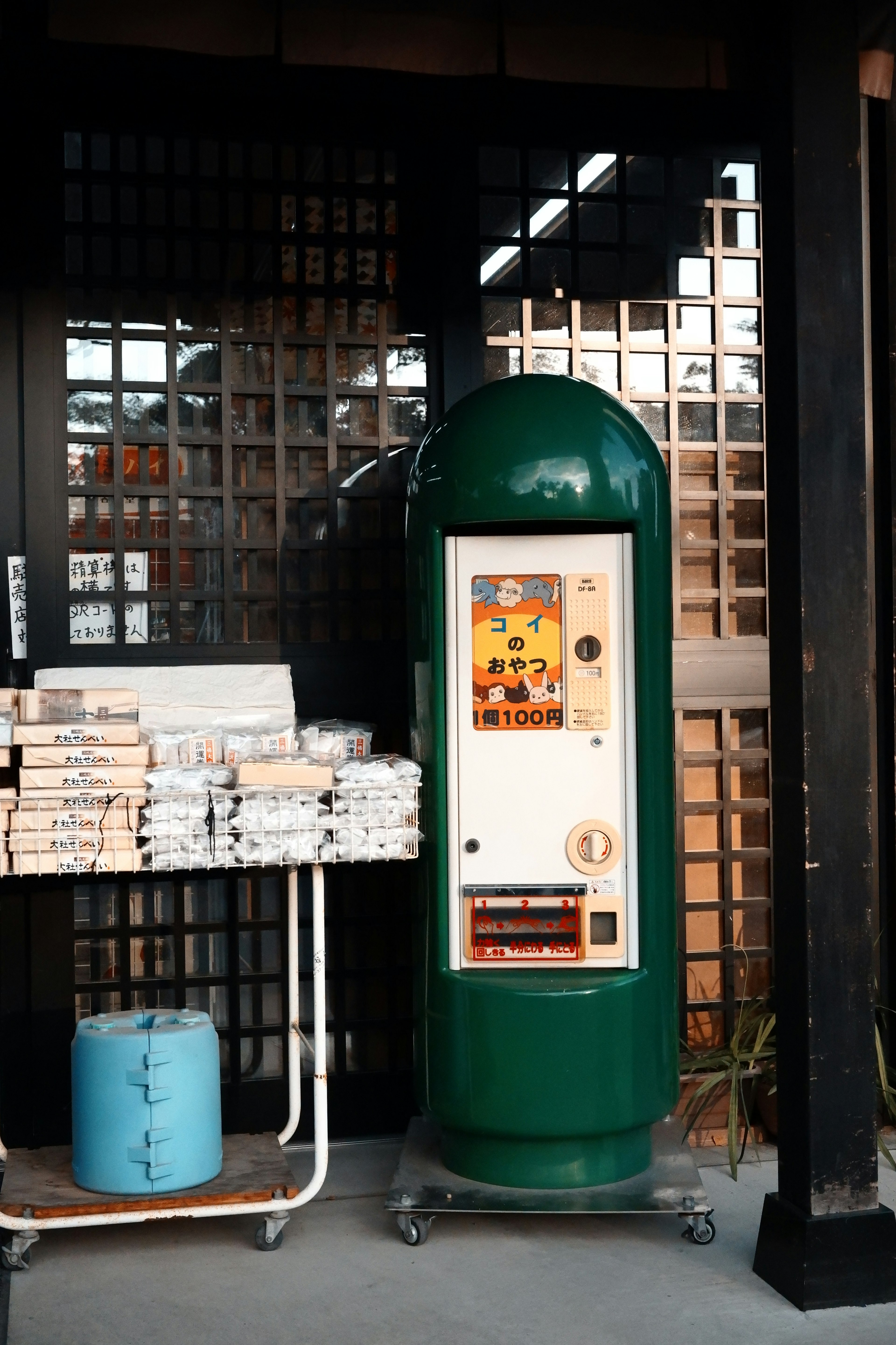 Distributore automatico verde accanto a una pila di giornali in un angolo di strada giapponese