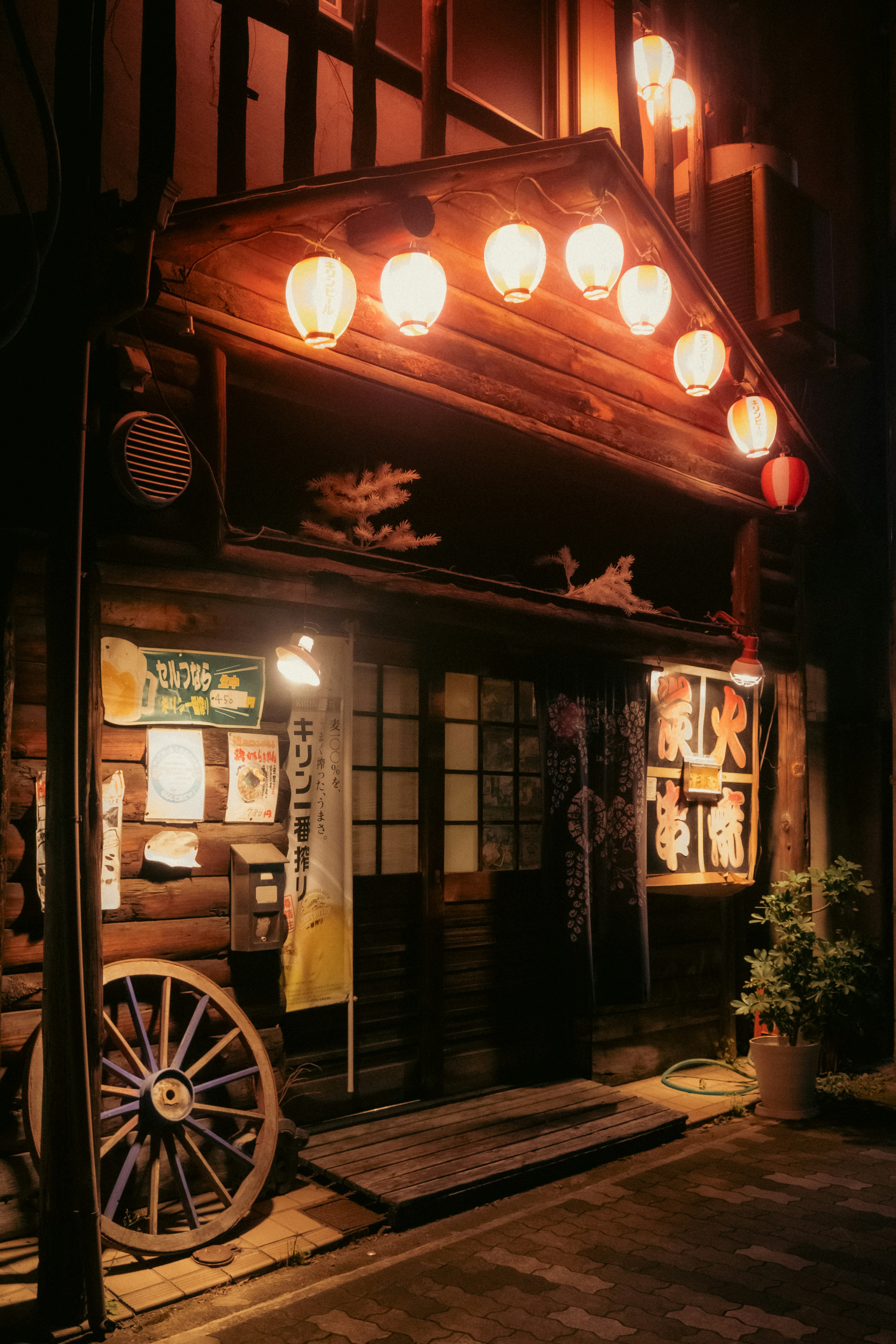 Traditional wooden Japanese restaurant exterior with illuminated lanterns and an old cart