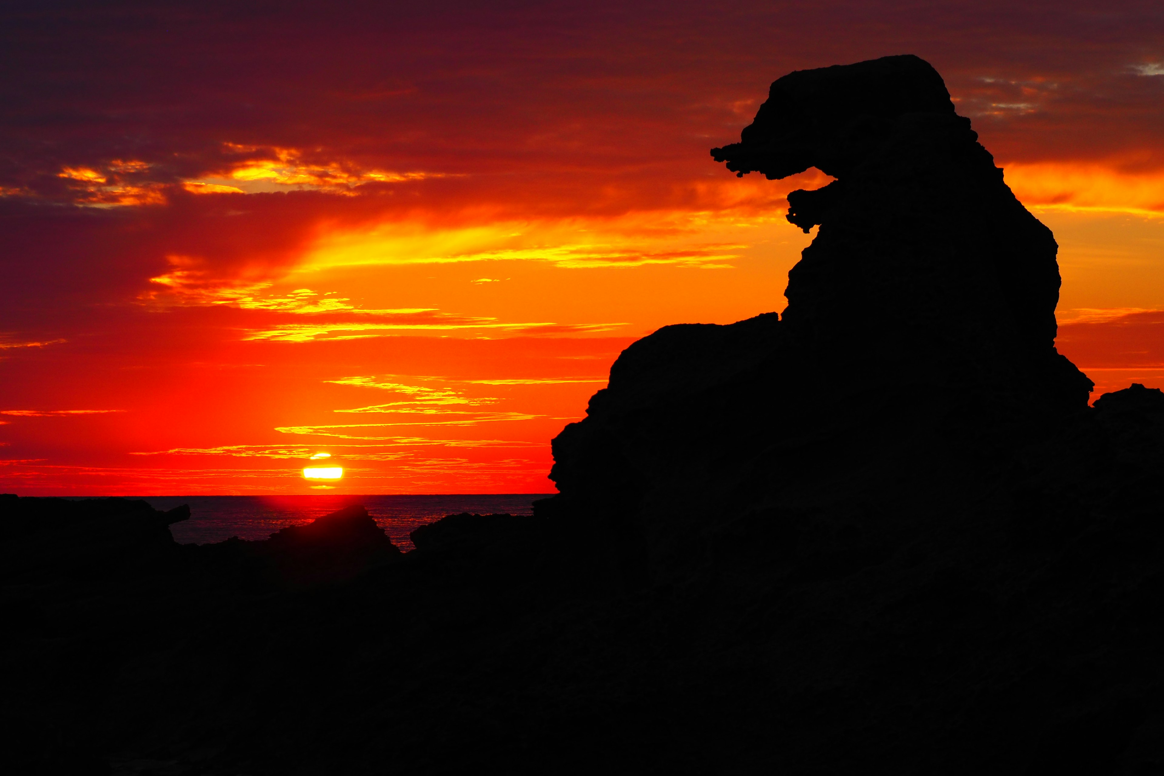 Eine wunderschöne Landschaft mit einer Silhouette eines Felsens, der einem Tier ähnelt, vor einem Sonnenuntergang