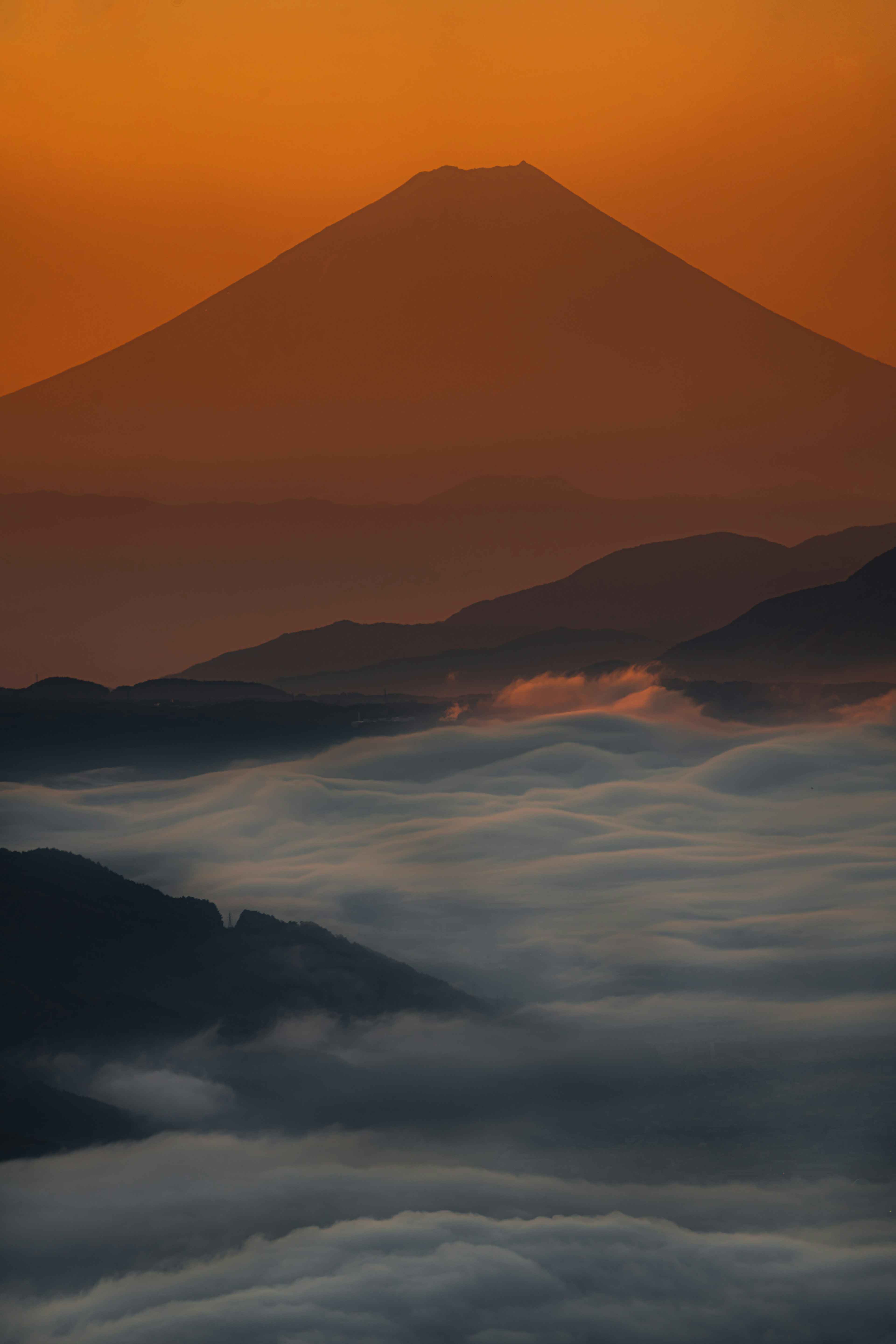 Silueta de montaña contra un atardecer naranja con un mar de nubes