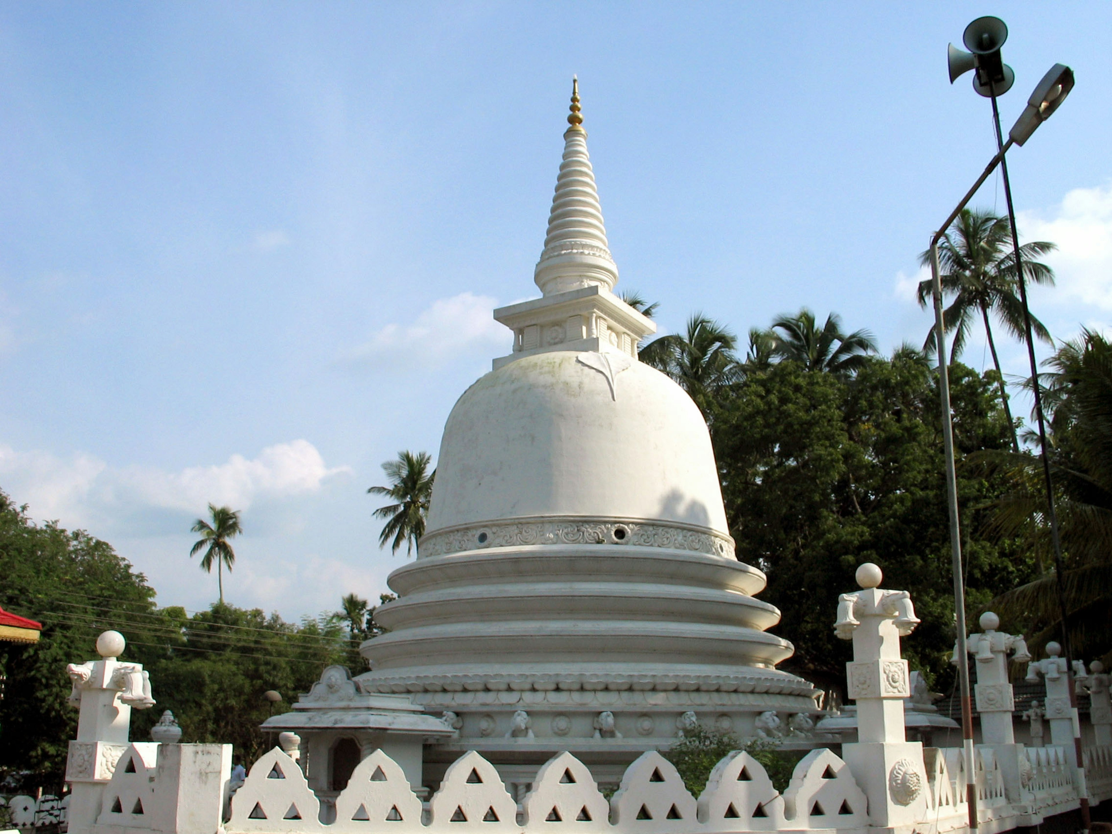 Stupa putih di bawah langit biru dikelilingi pepohonan