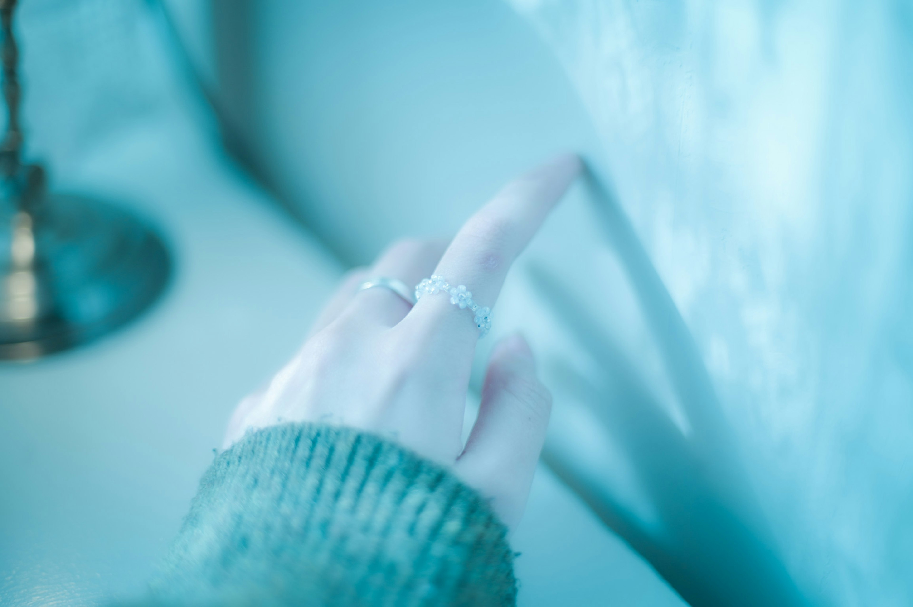 A hand with rings touching a wall in a soft blue light