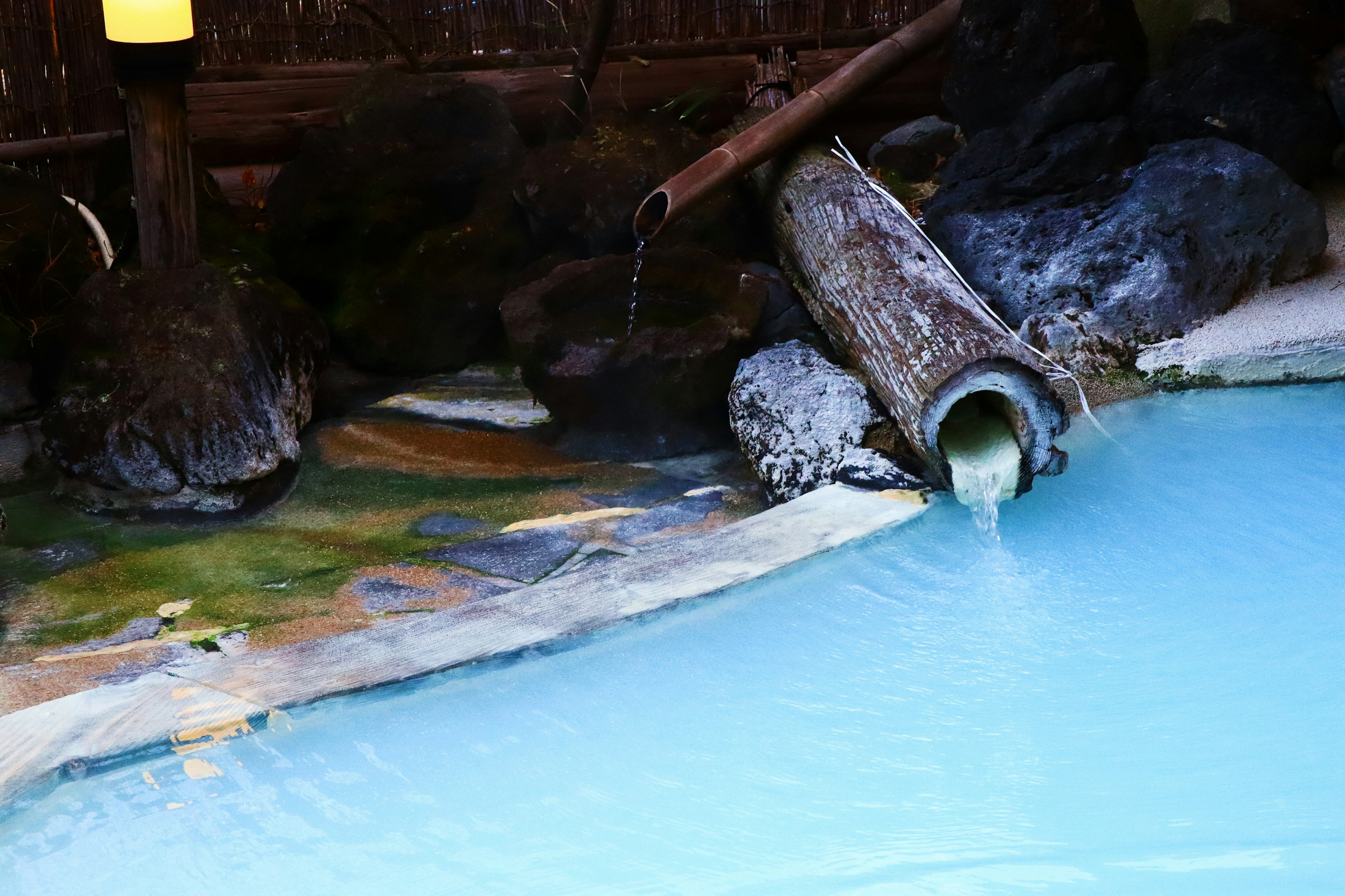 青い温泉水と木製の水流パイプがある風景