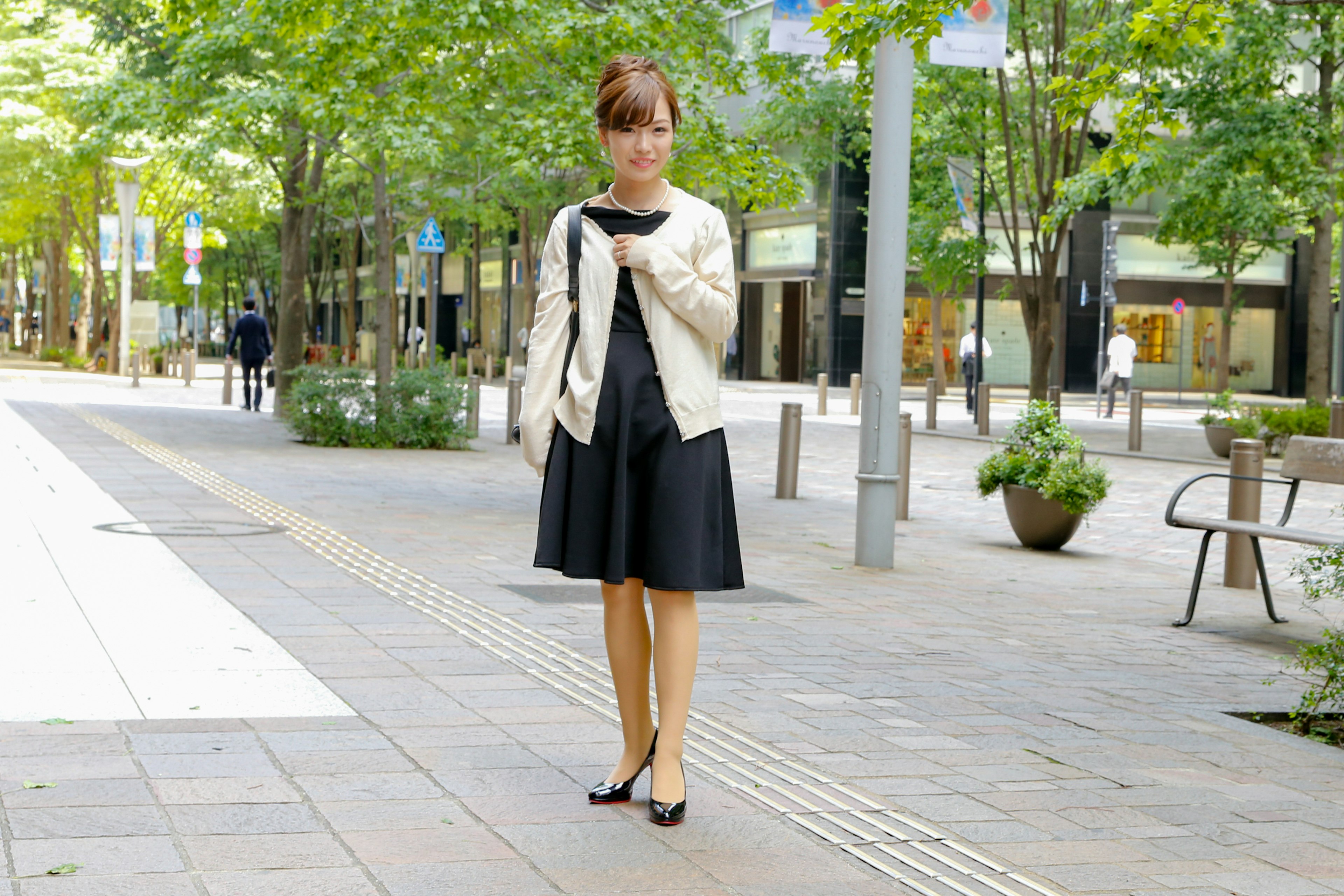 A woman wearing a black dress and white jacket standing in an urban setting