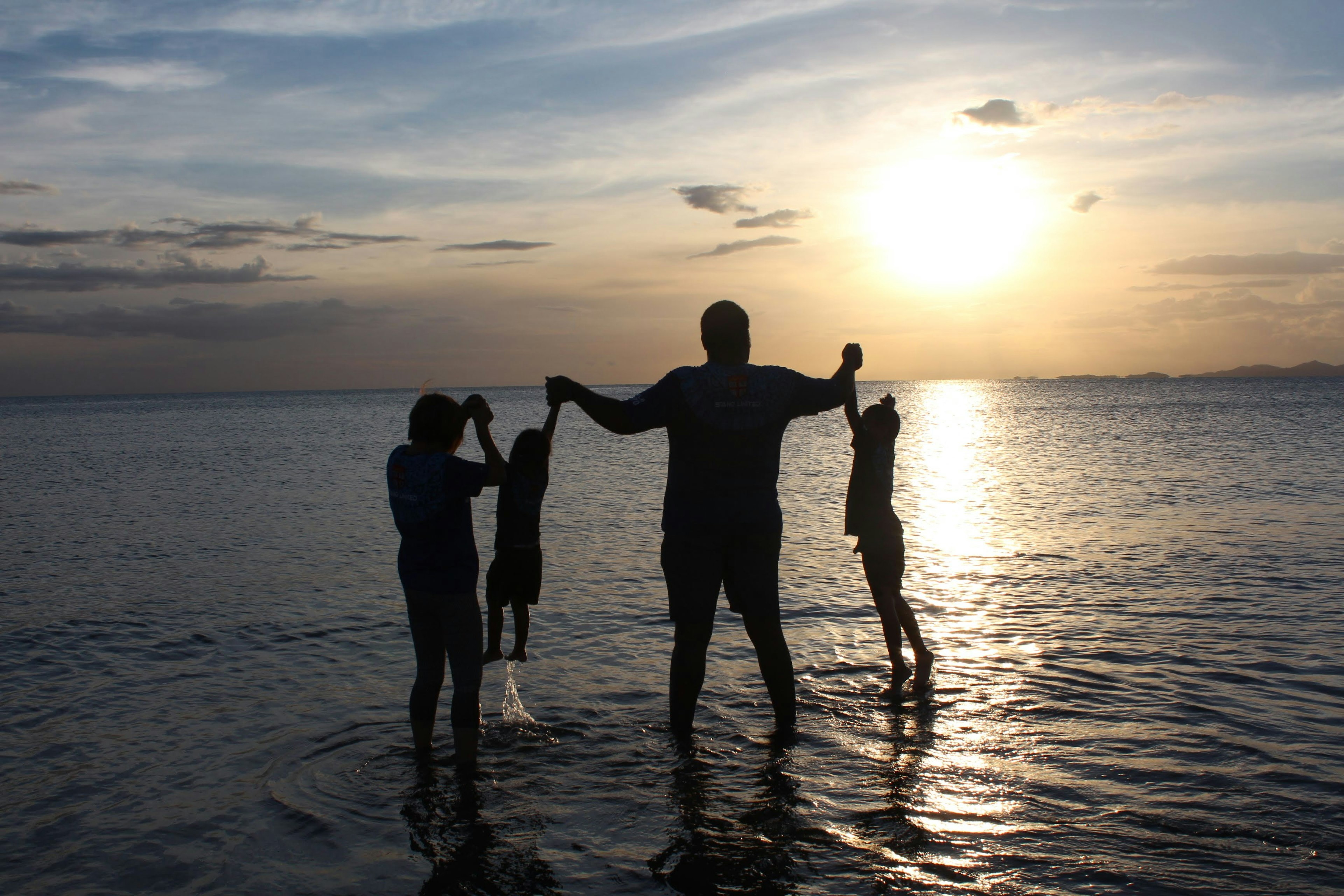 Silhouette d'une famille jouant avec des enfants sur la plage au coucher du soleil