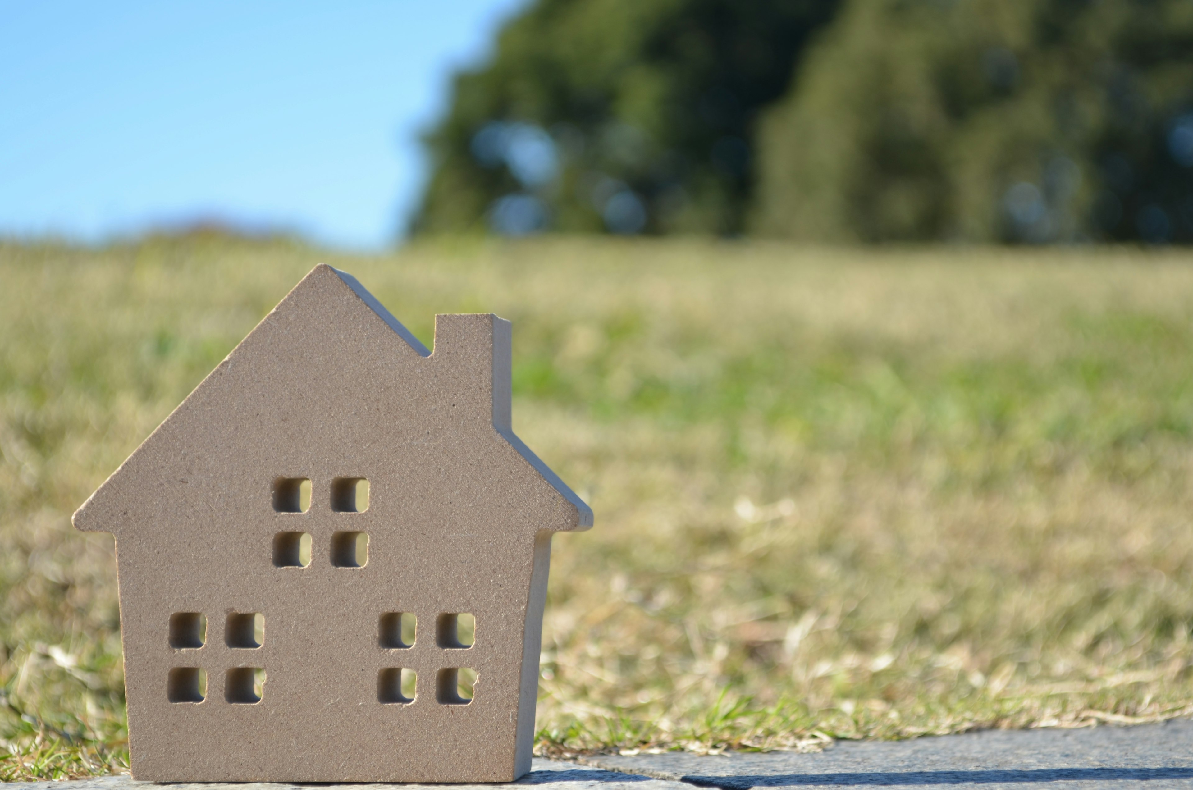 Piccolo modello di casa in cartone posizionato di fronte a un campo erboso