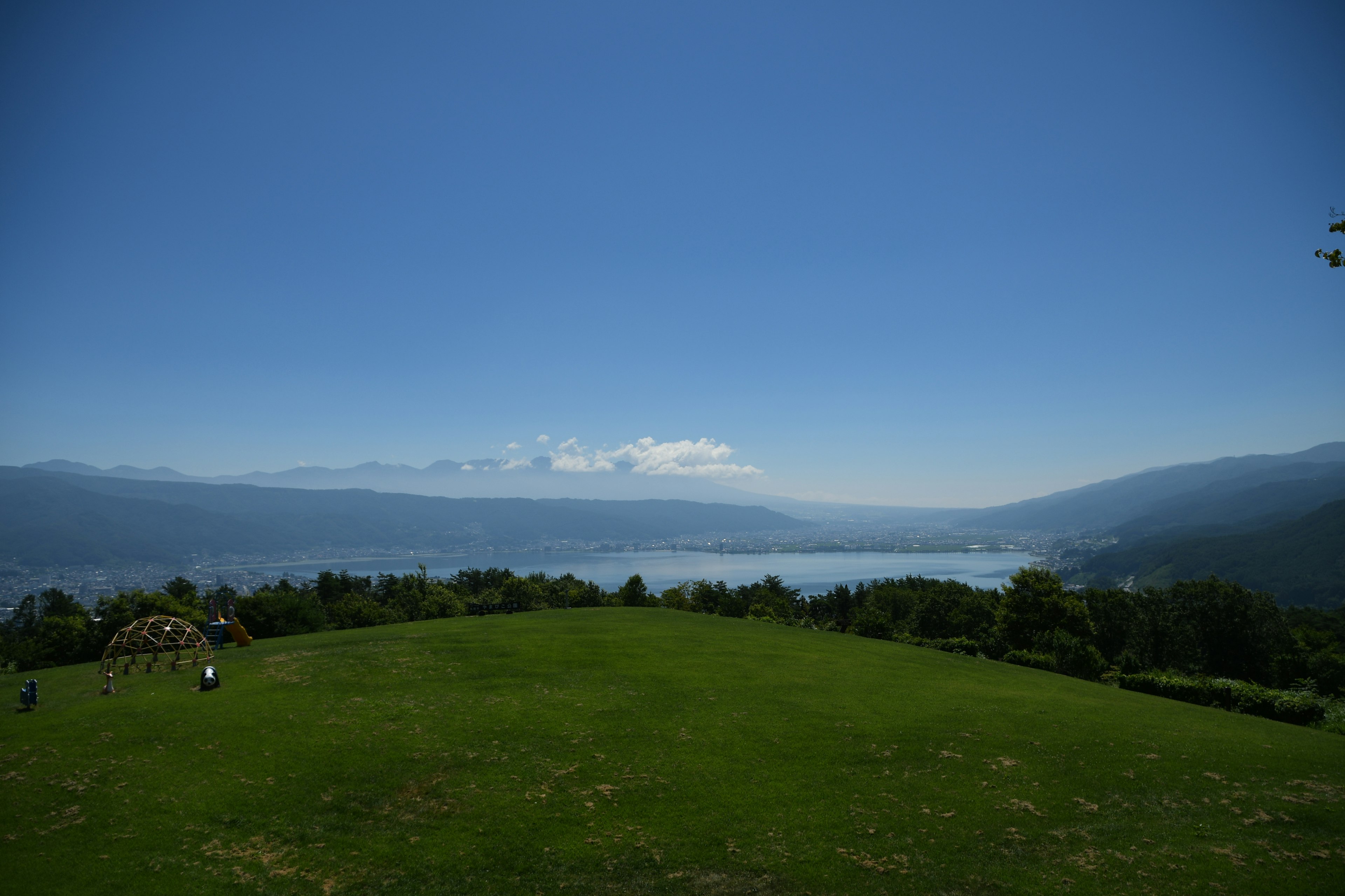 Vista escénica de una colina verde con vista a un lago y cielo azul