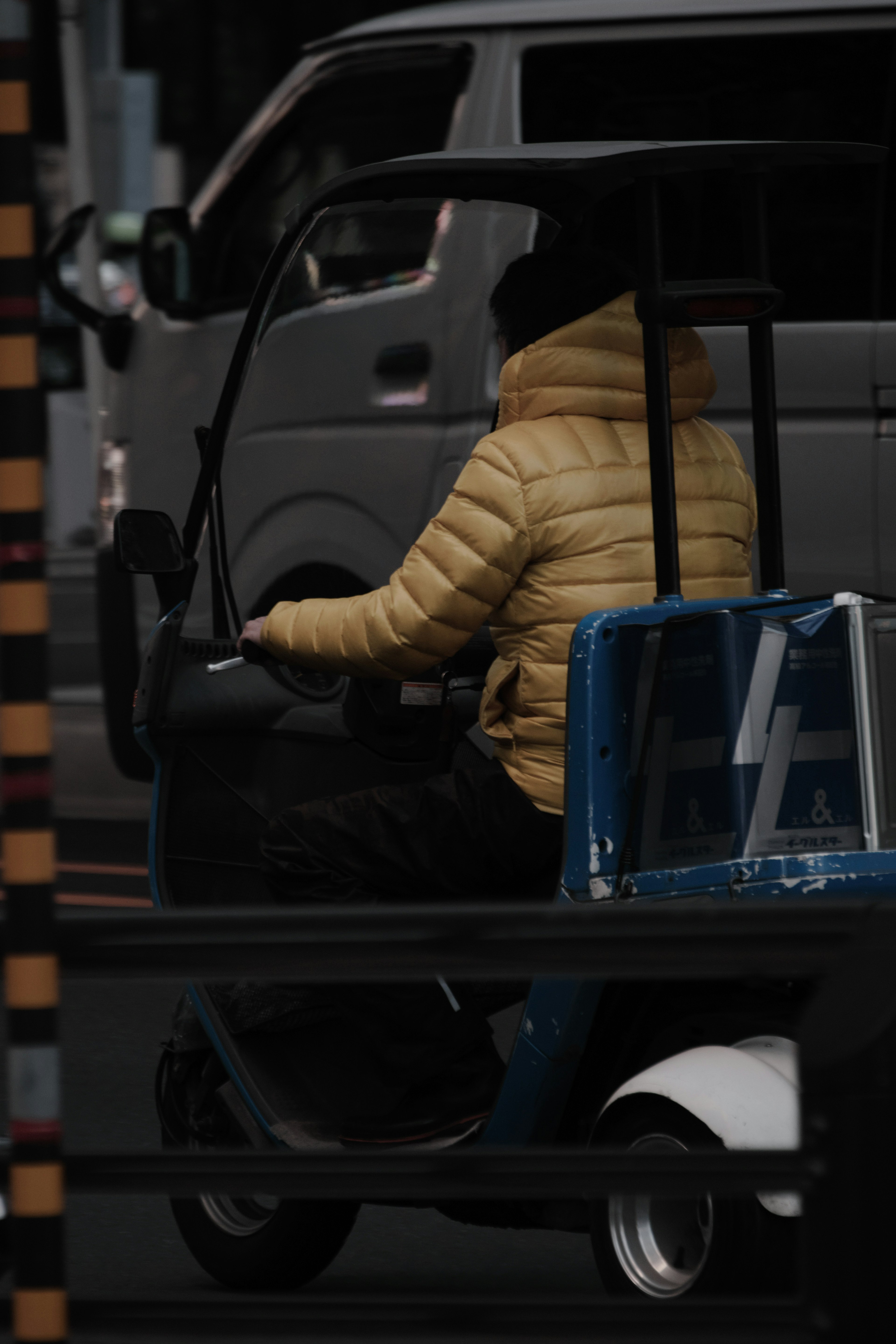 A person wearing a yellow puffer jacket riding a golf cart against a dark background