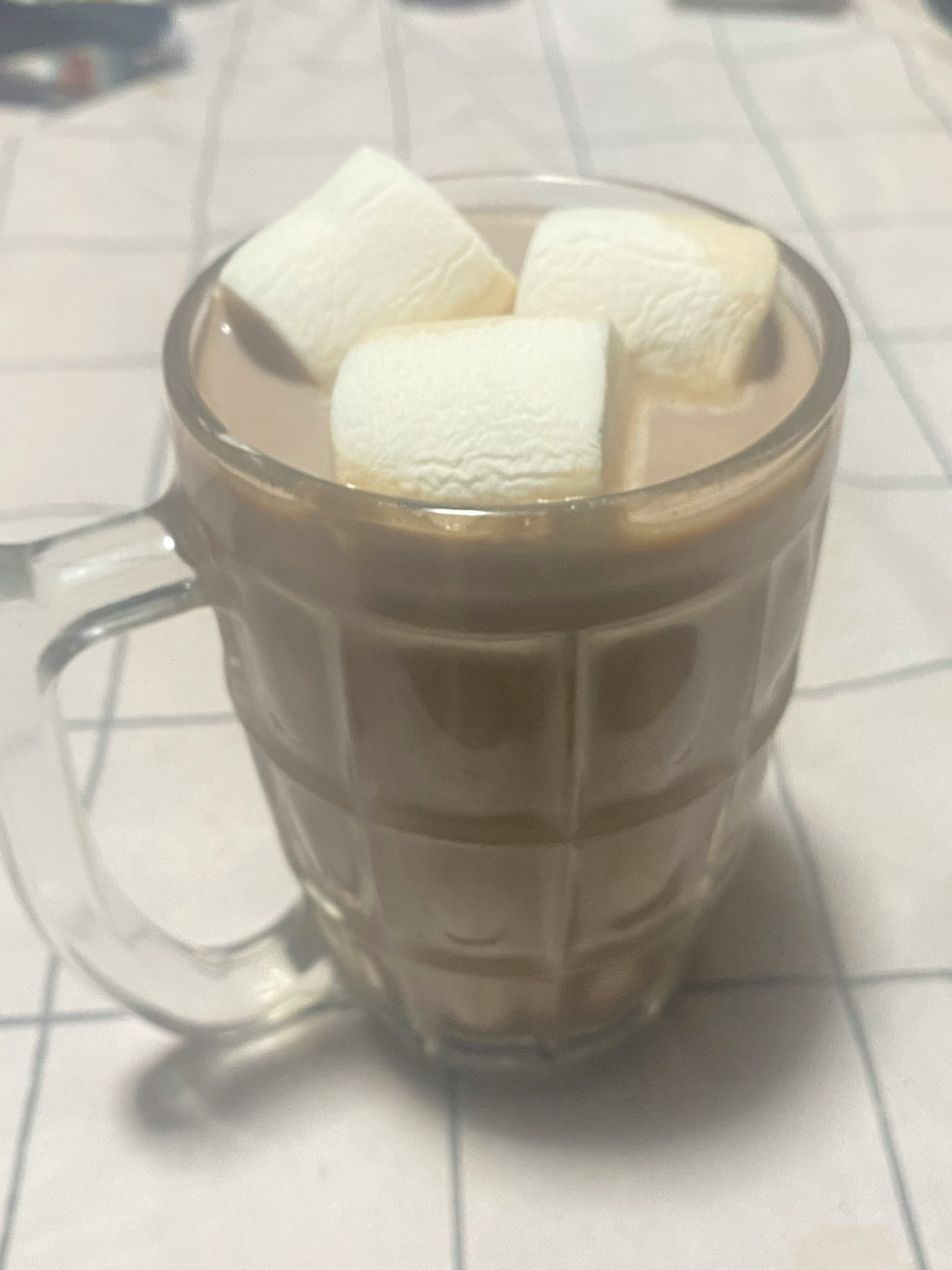 A clear glass of hot chocolate topped with marshmallows