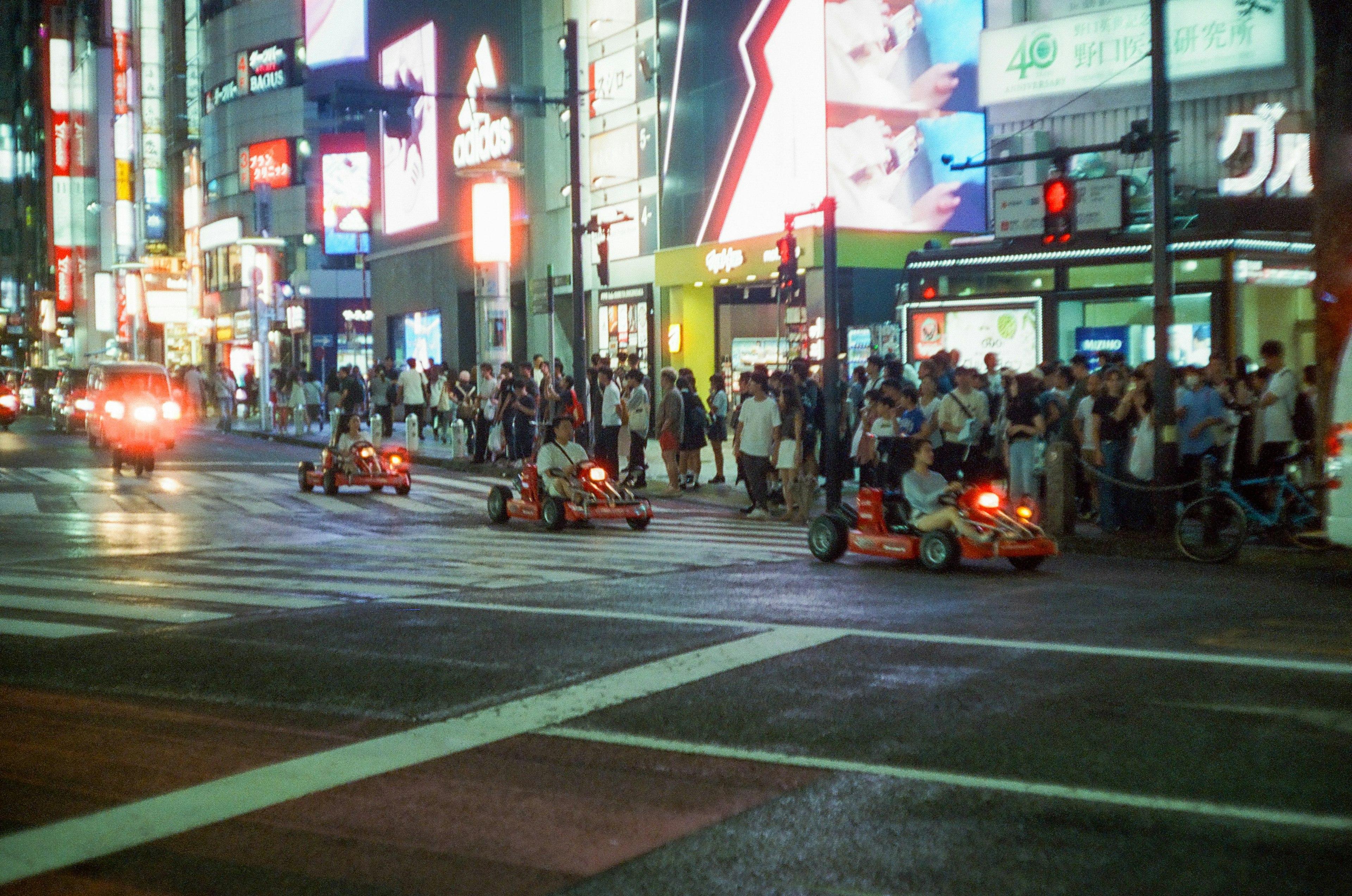 Go-Karts fahren in einer belebten Straße in Tokio bei Nacht mit Menschenmengen