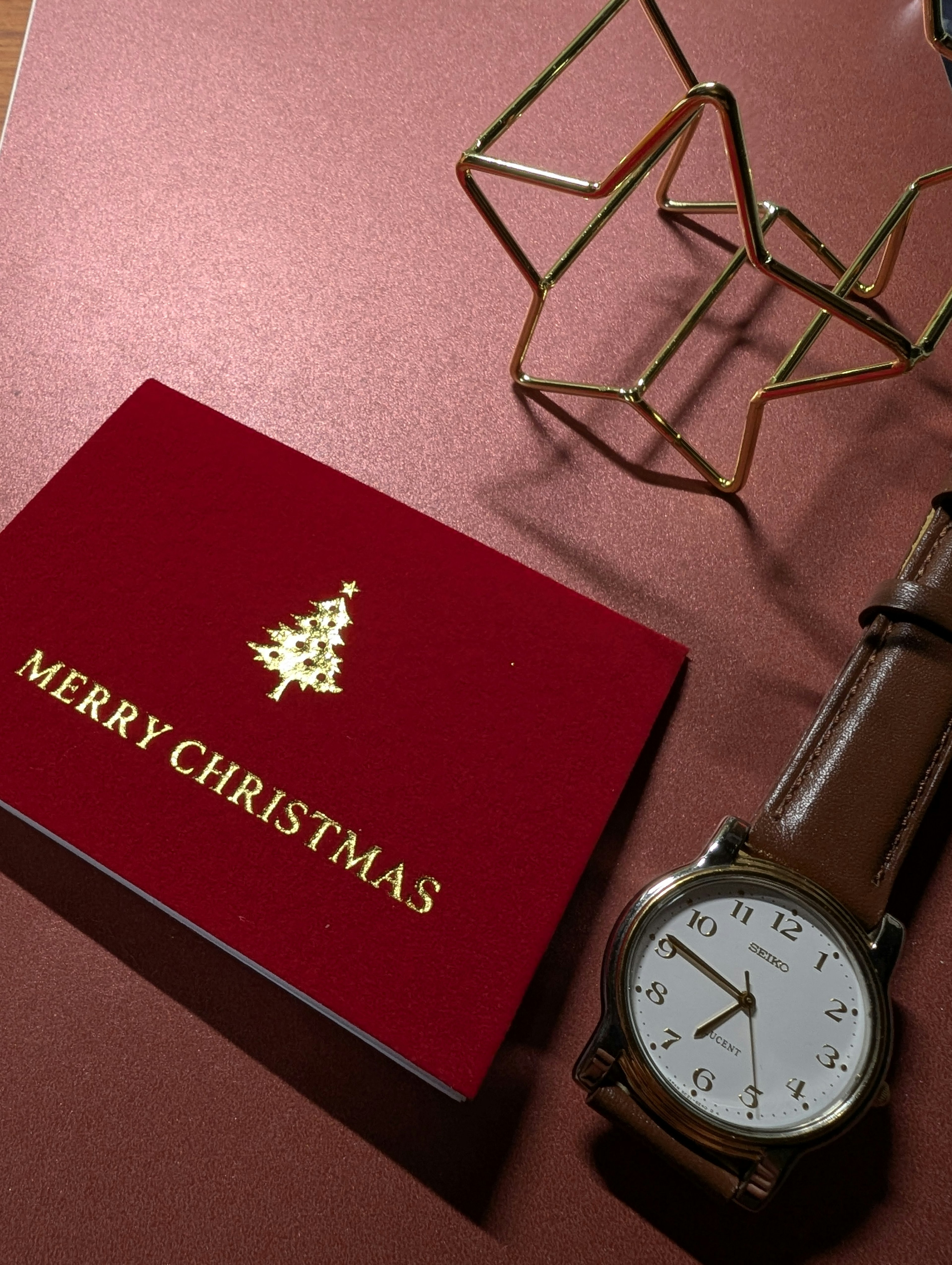 Tarjeta de Navidad roja con diseño de árbol dorado y un reloj sobre una superficie marrón