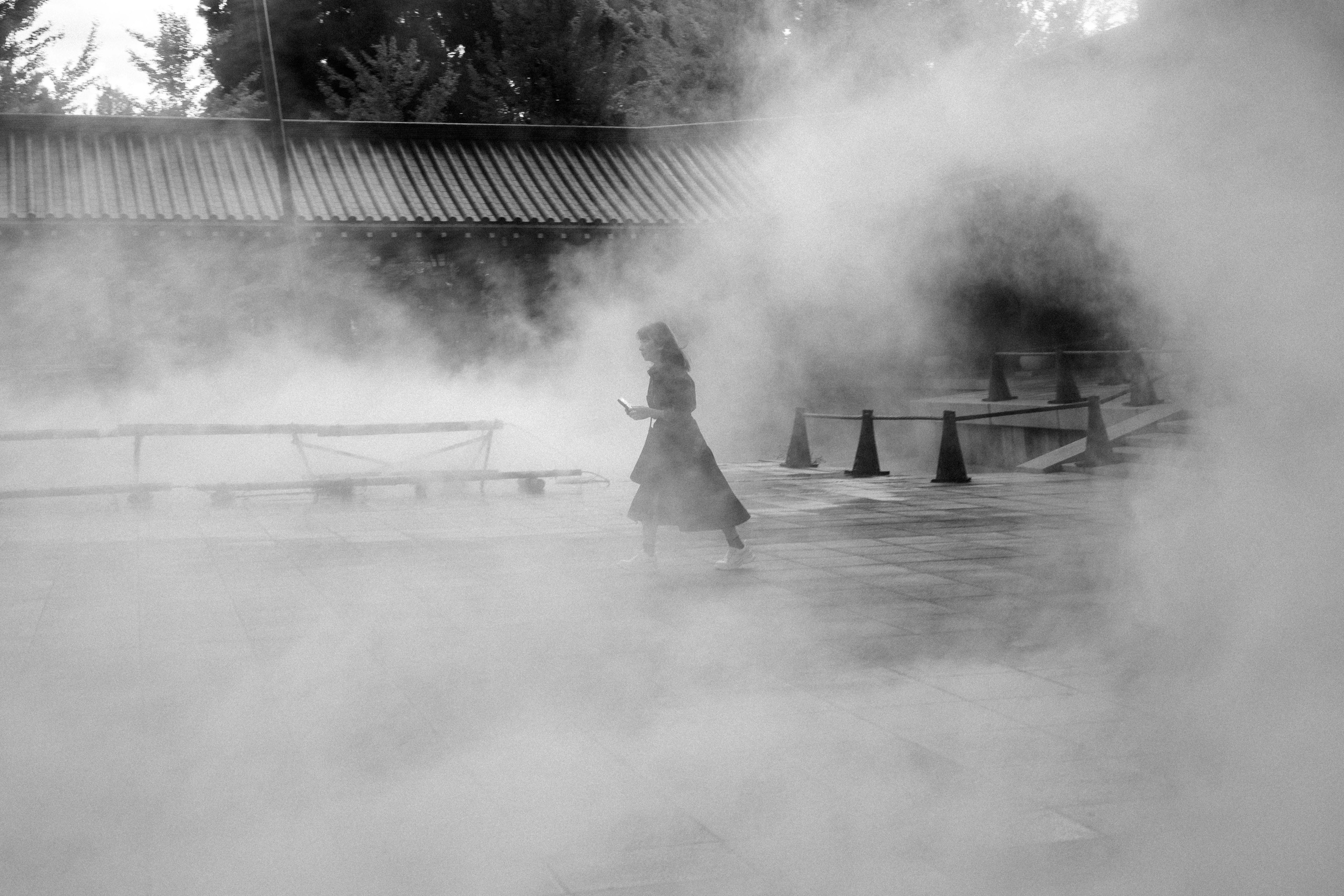 Silhouette di una donna che cammina nella nebbia con un edificio sullo sfondo