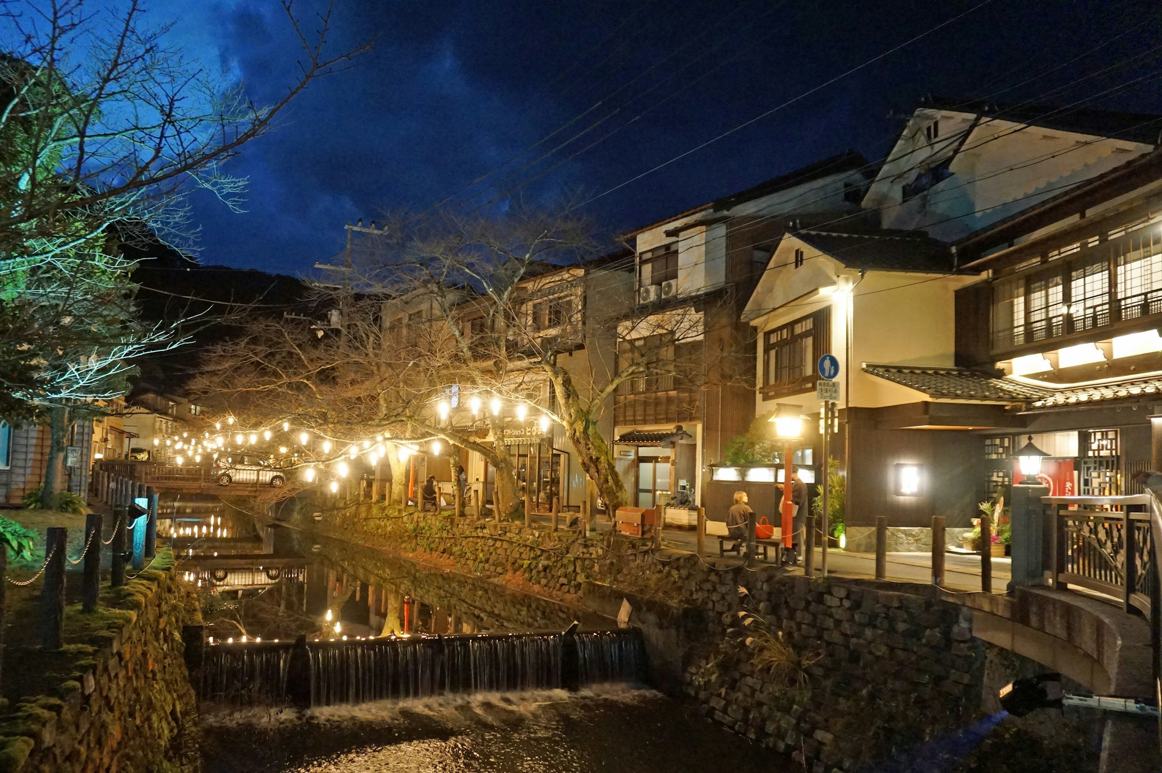 Traditionelle japanische Häuser entlang eines Flusses bei Nacht mit warmen dekorativen Lichtern