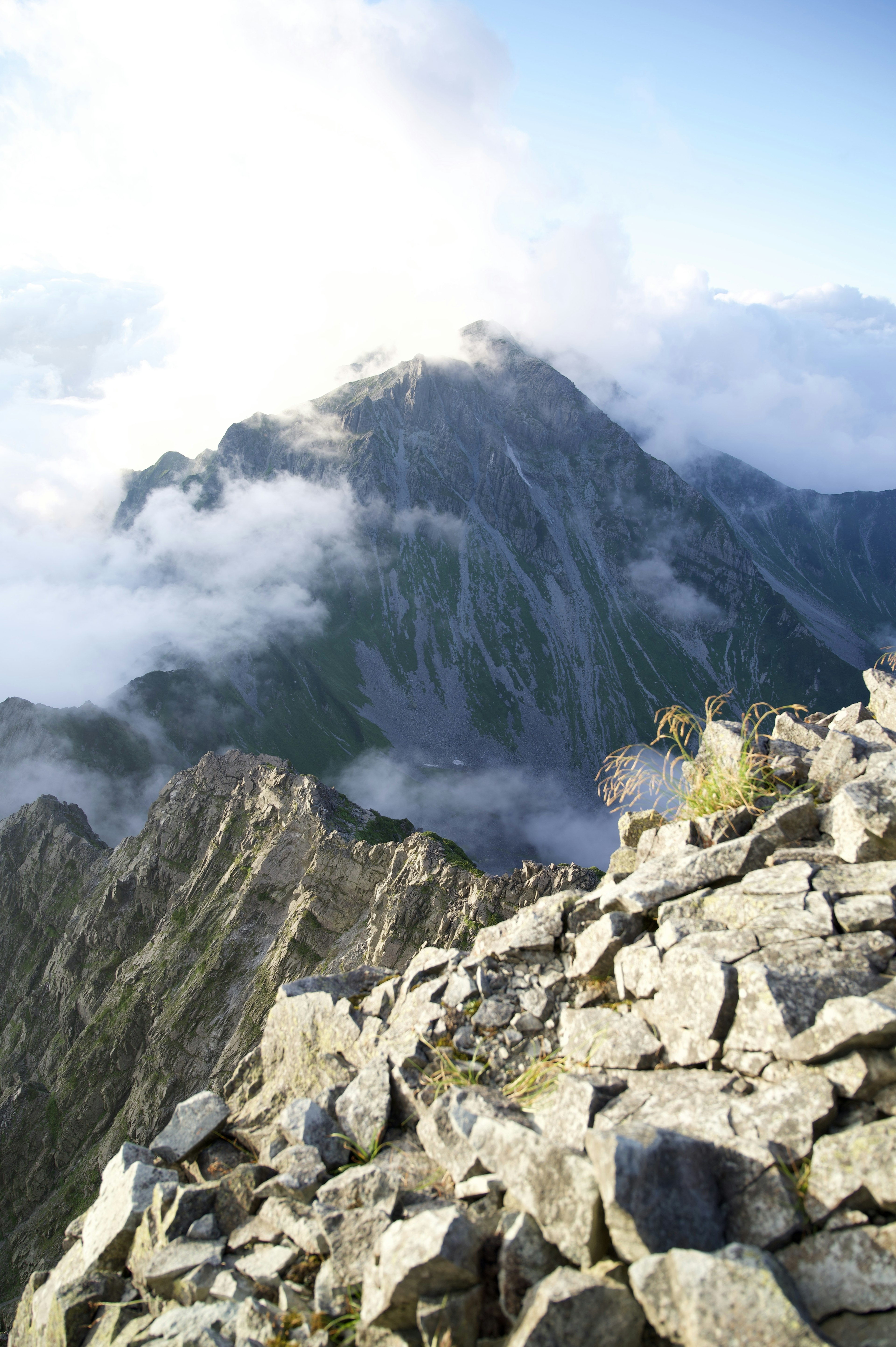 Vista dalla cima della montagna con terreno roccioso e cime coperte di nuvole