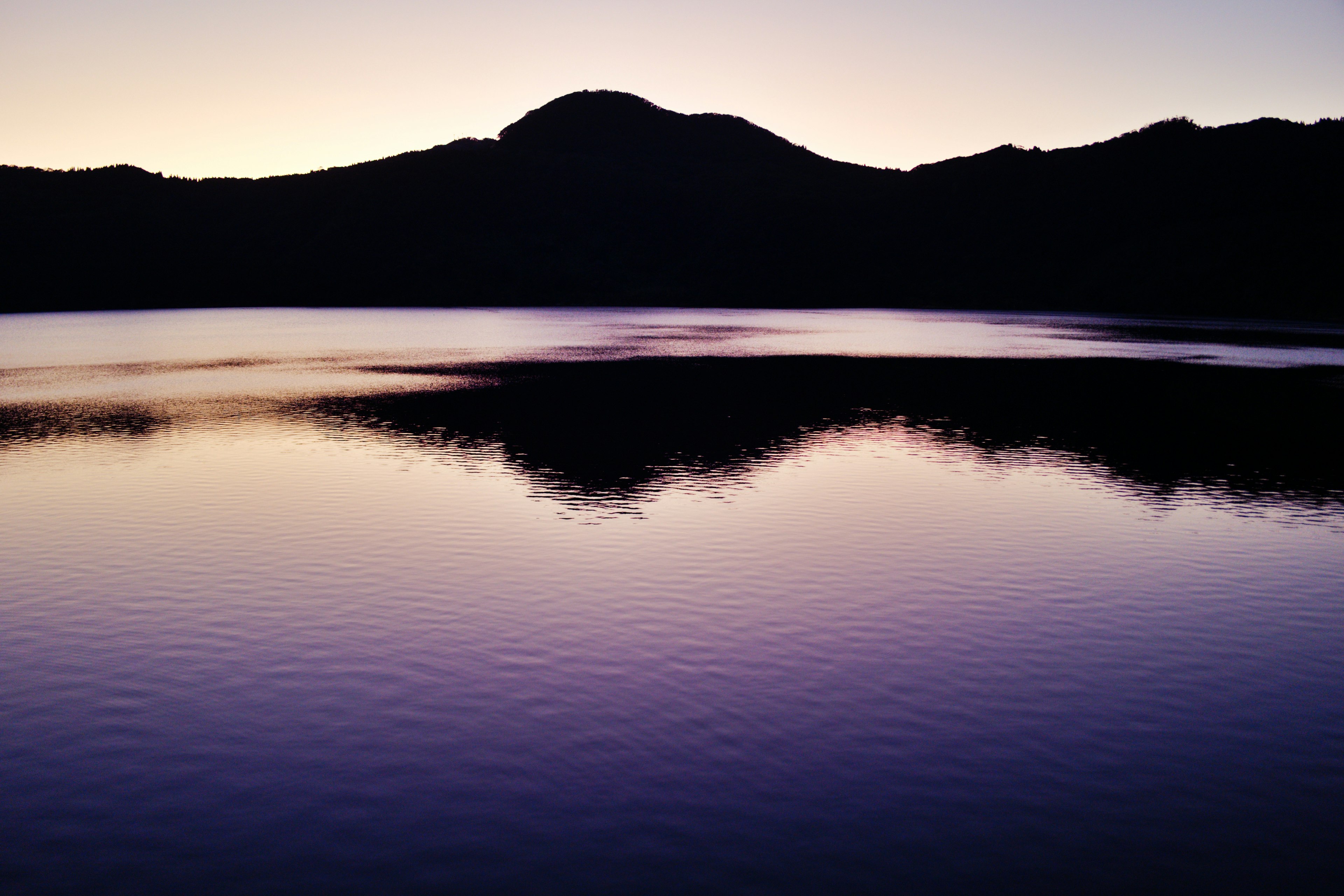 Lago tranquilo con montañas en silueta reflejando tonos morados al atardecer