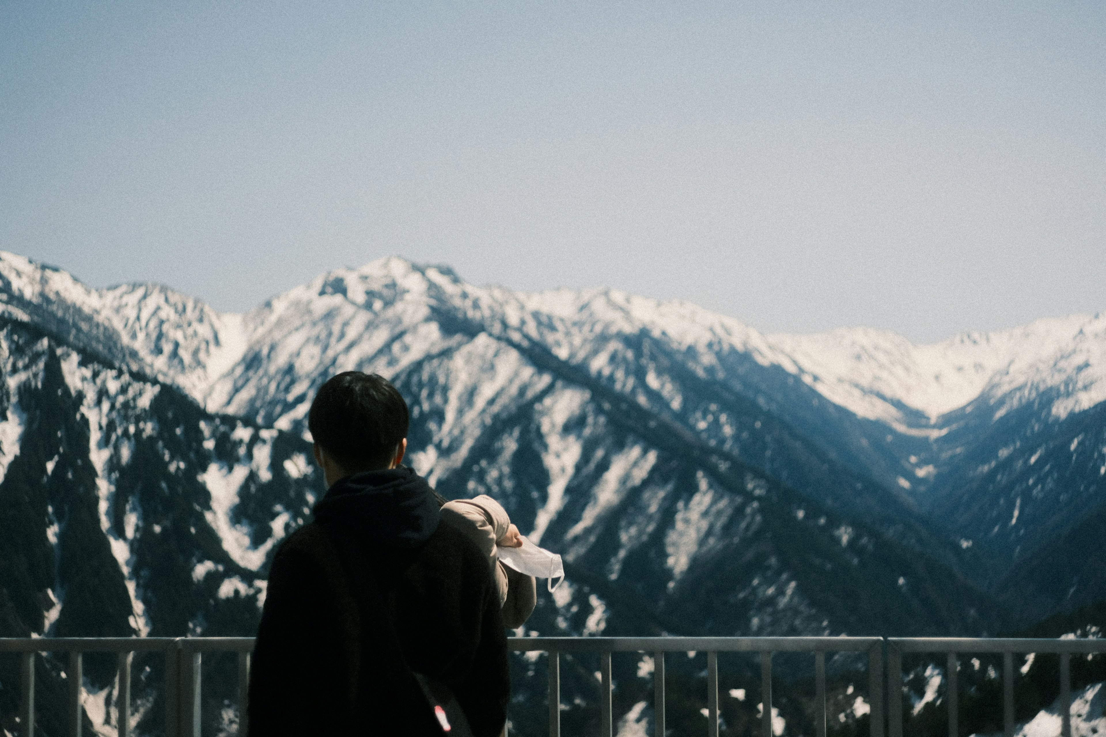 A person standing with their back to the camera overlooking snow-covered mountains