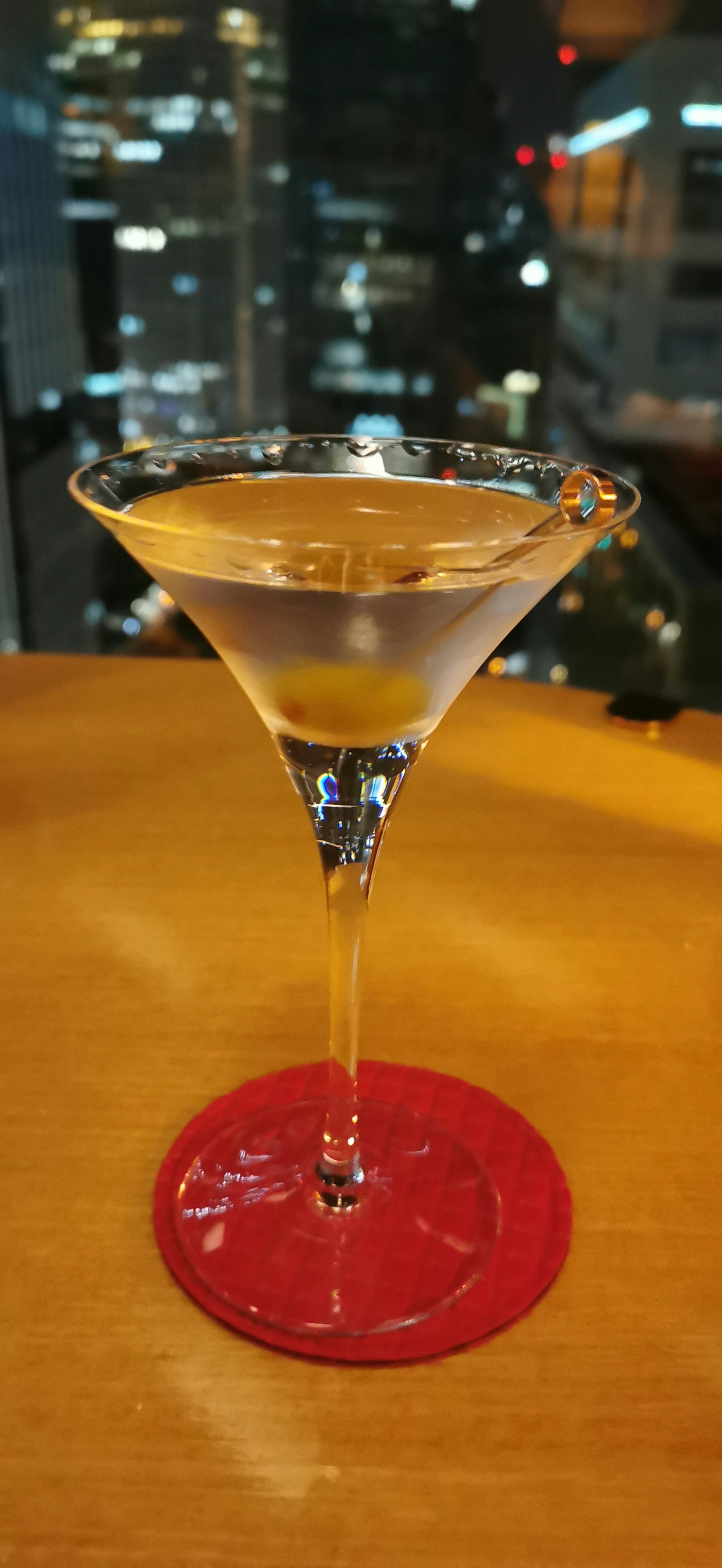 Cocktail glass with drink on a red coaster and city skyline at night