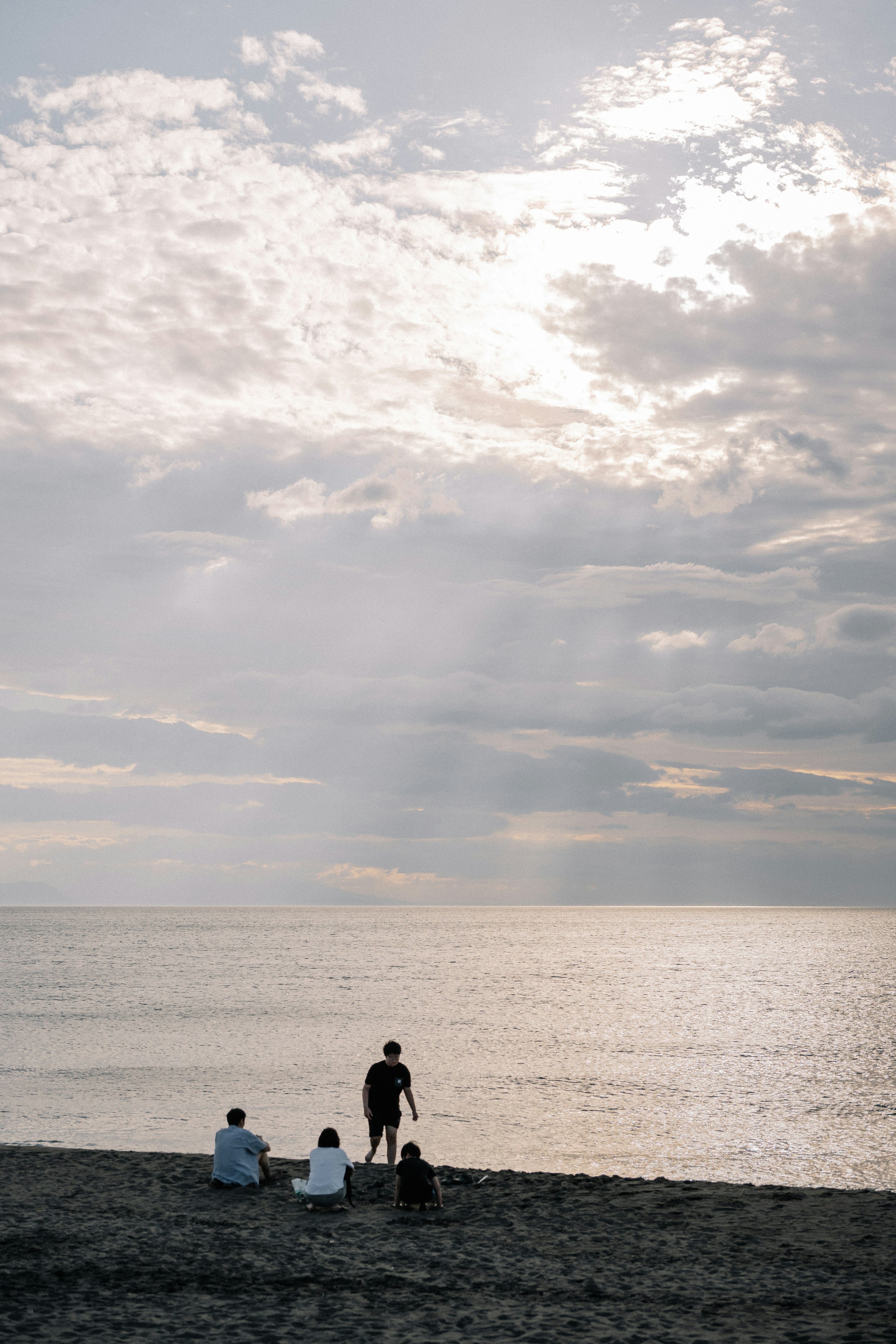 Gruppo di persone che osservano il tramonto sulla spiaggia con cielo nuvoloso