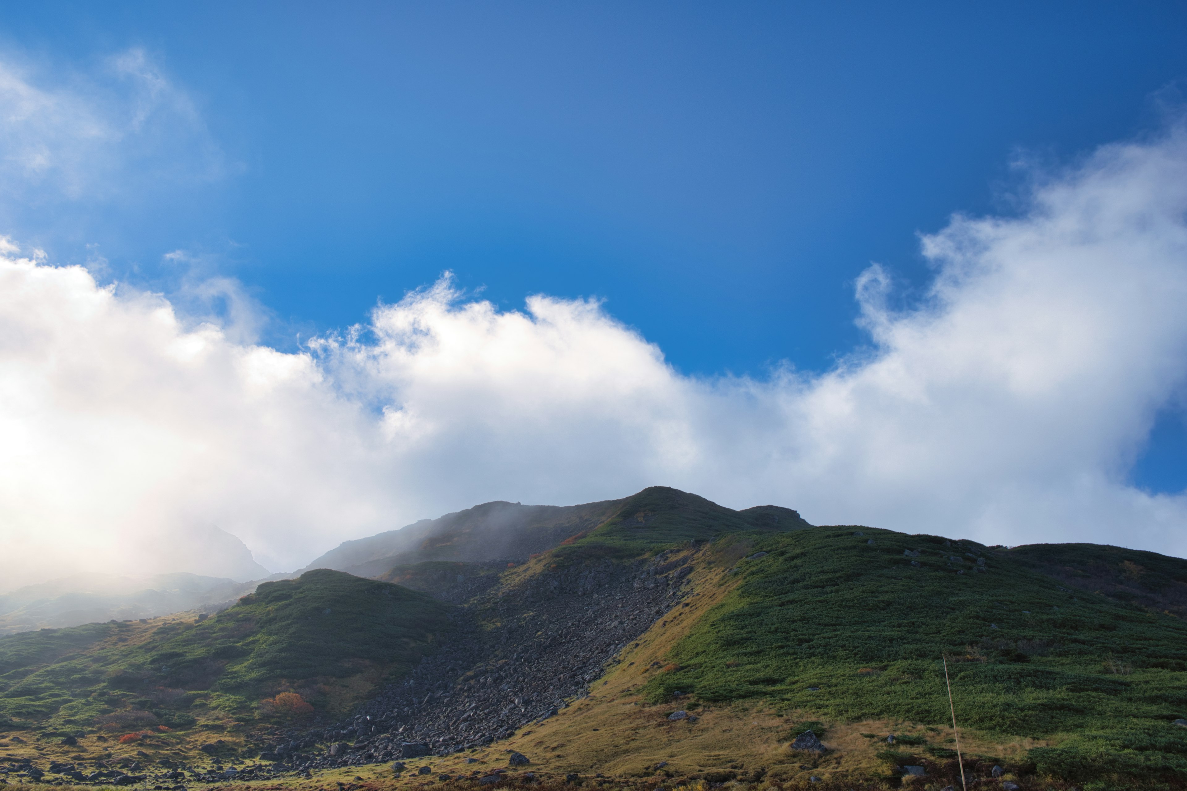 Paesaggio montano verde sotto un cielo blu e nuvole bianche