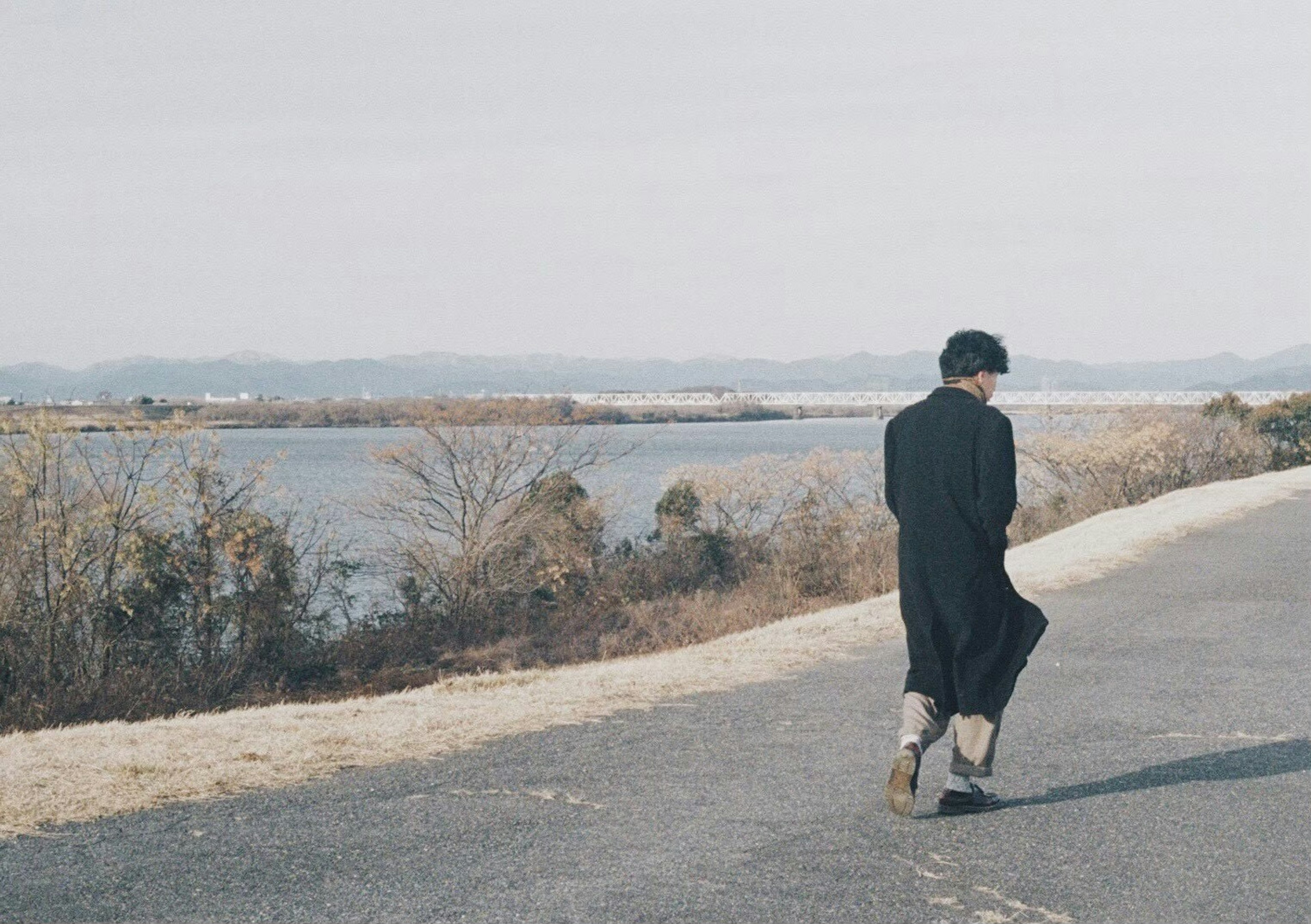 A person walking along a riverside path the landscape is calm and serene