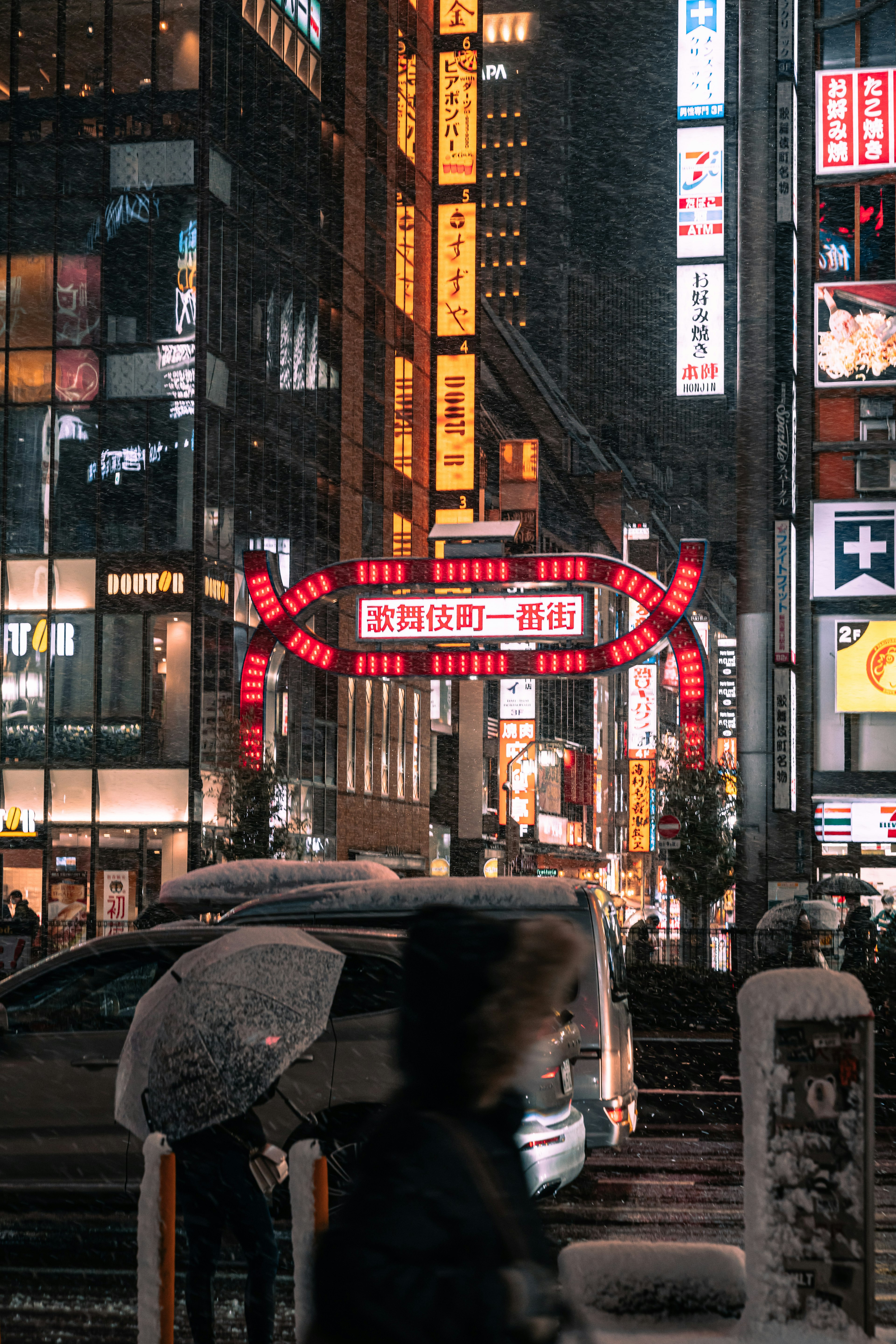 Scène urbaine sous la neige avec des enseignes au néon et des bâtiments comportant des personnes avec des parapluies