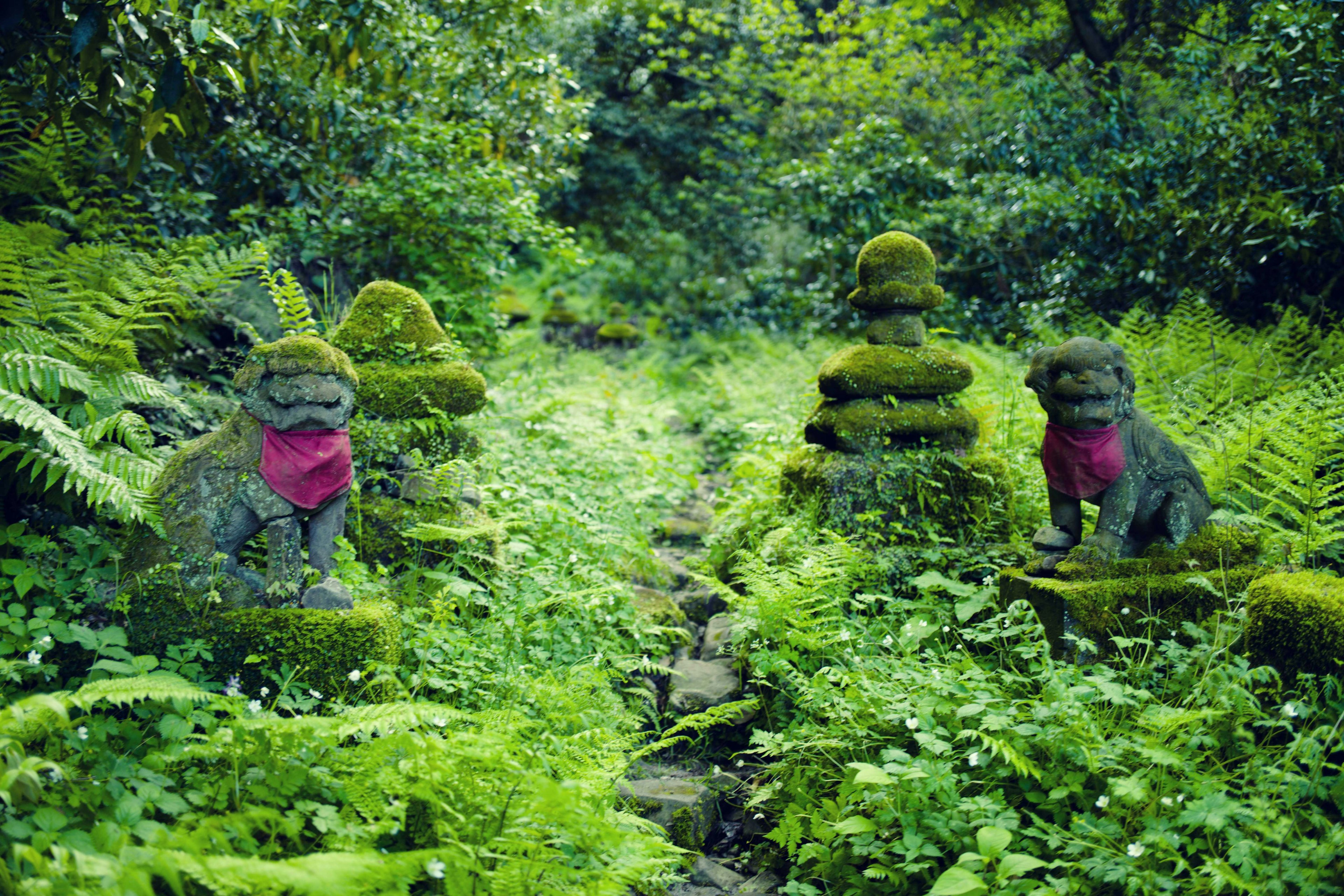 緑の森に囲まれた苔むした石像と石の塔が並んでいる様子