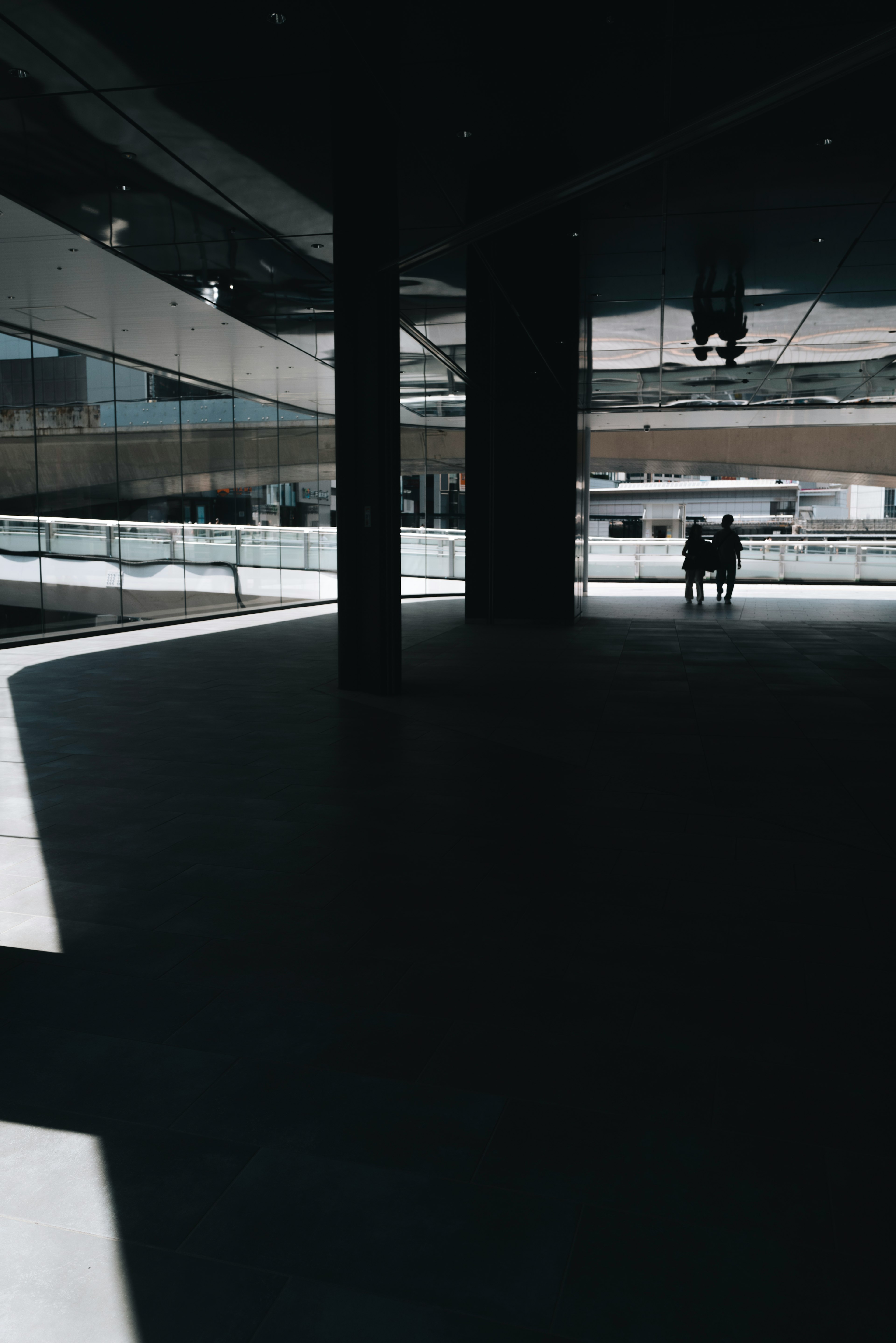 Un espace intérieur faiblement éclairé avec une seule personne et de grandes fenêtres créant des ombres frappantes