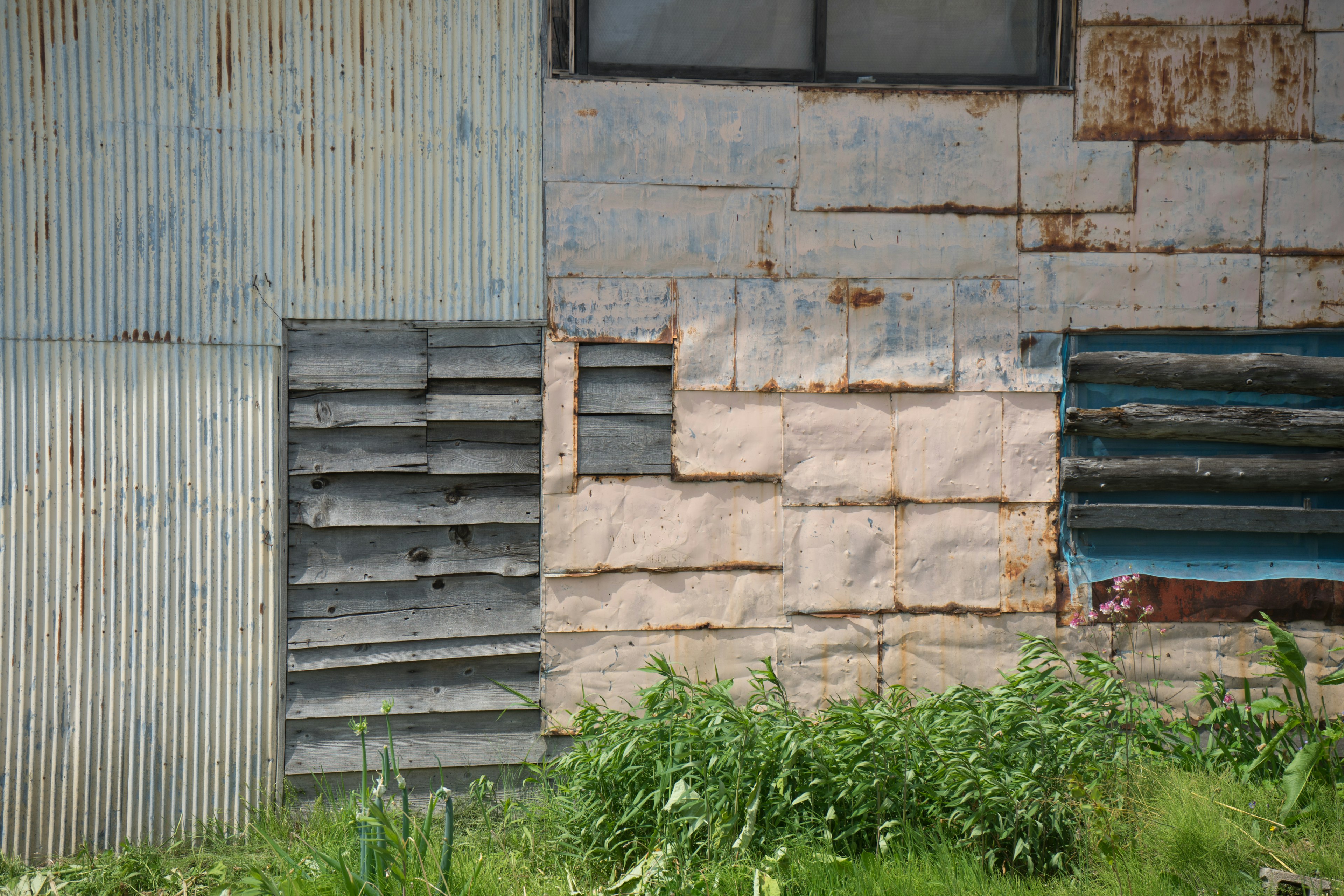 Collage de sections murales en métal et en bois avec une fenêtre et de l'herbe verte visible