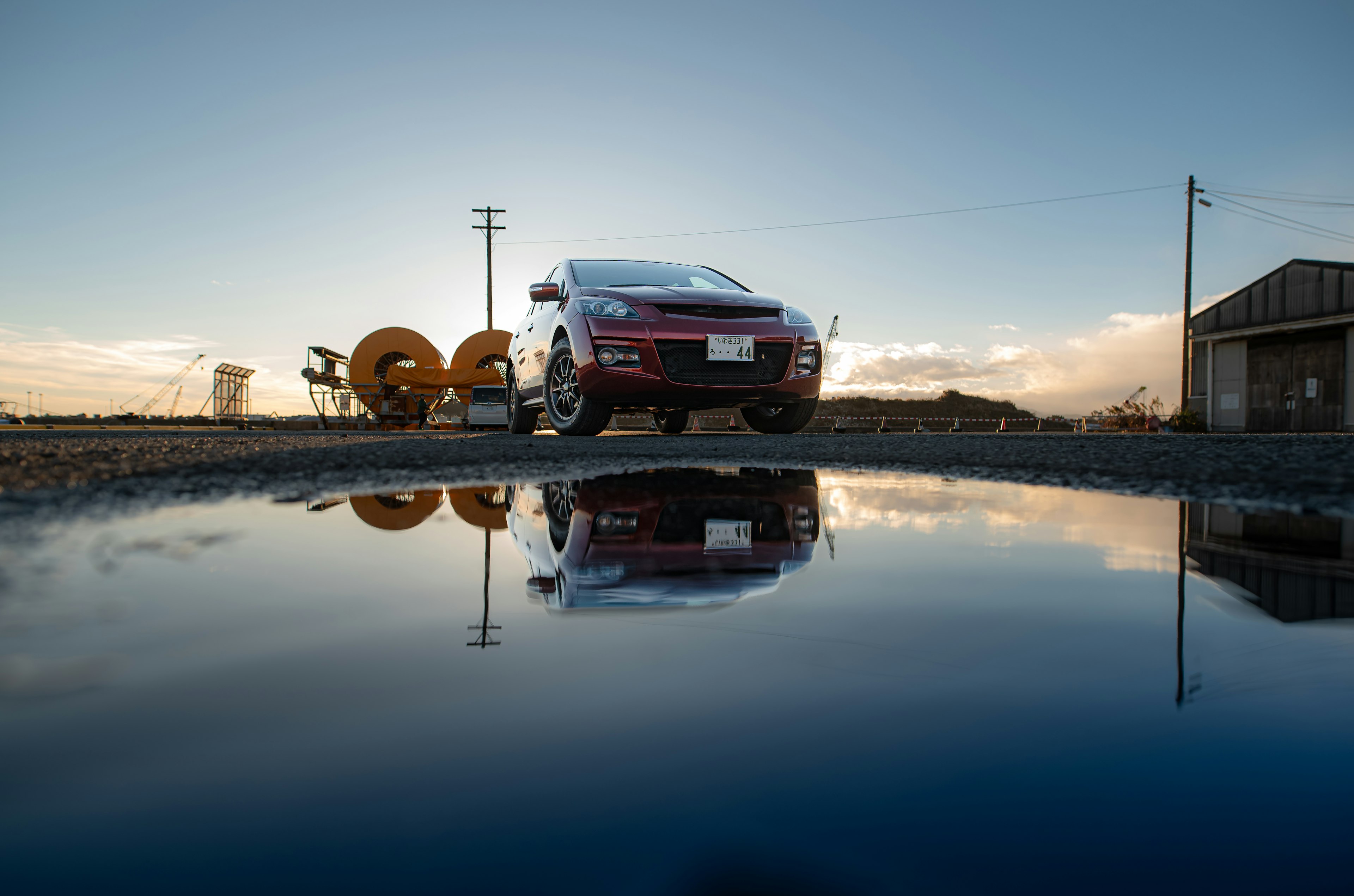 Voiture rouge réfléchie dans une flaque d'eau avec un coucher de soleil