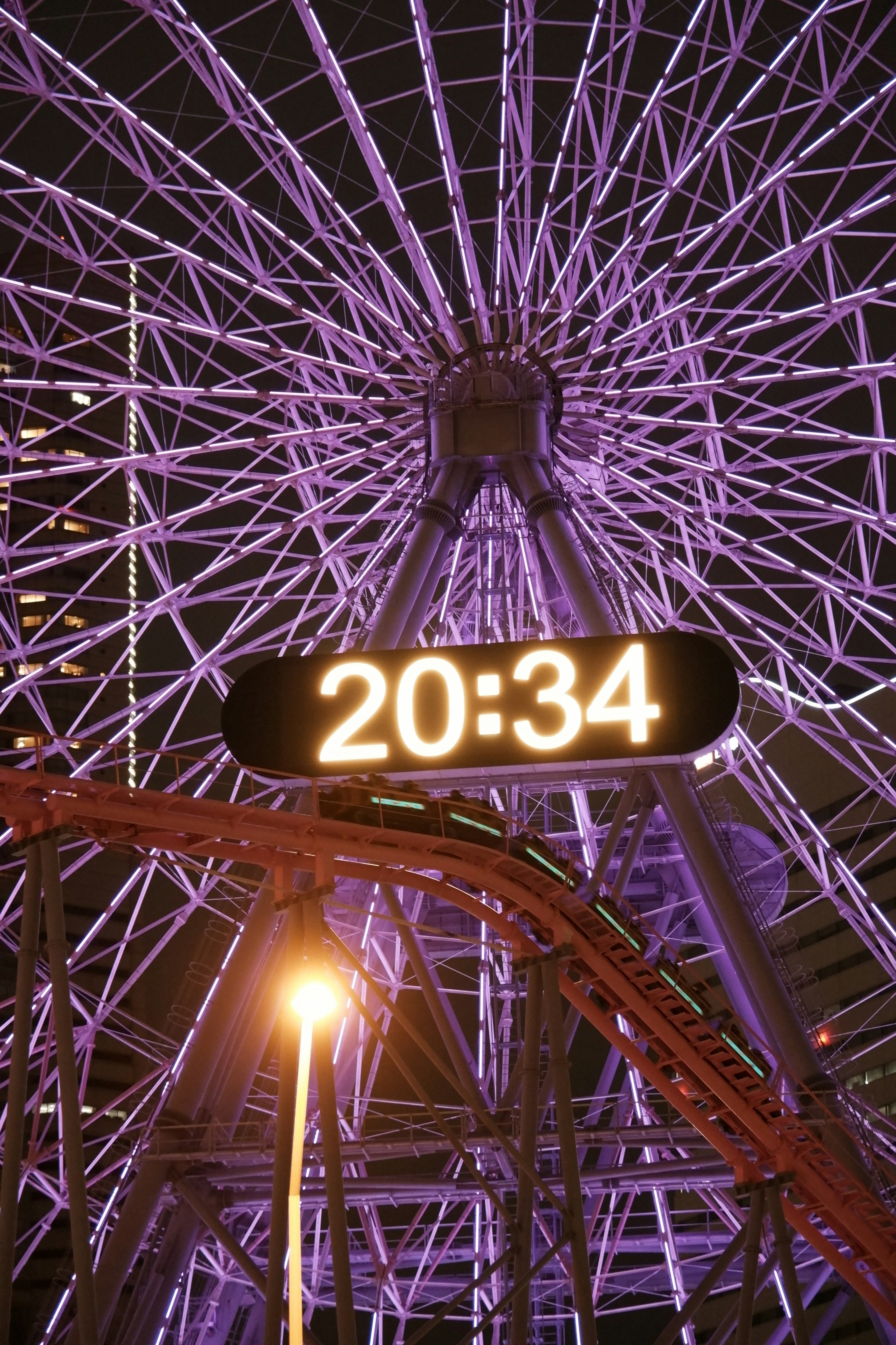 Rueda de la fortuna nocturna con luces moradas y reloj digital mostrando la hora