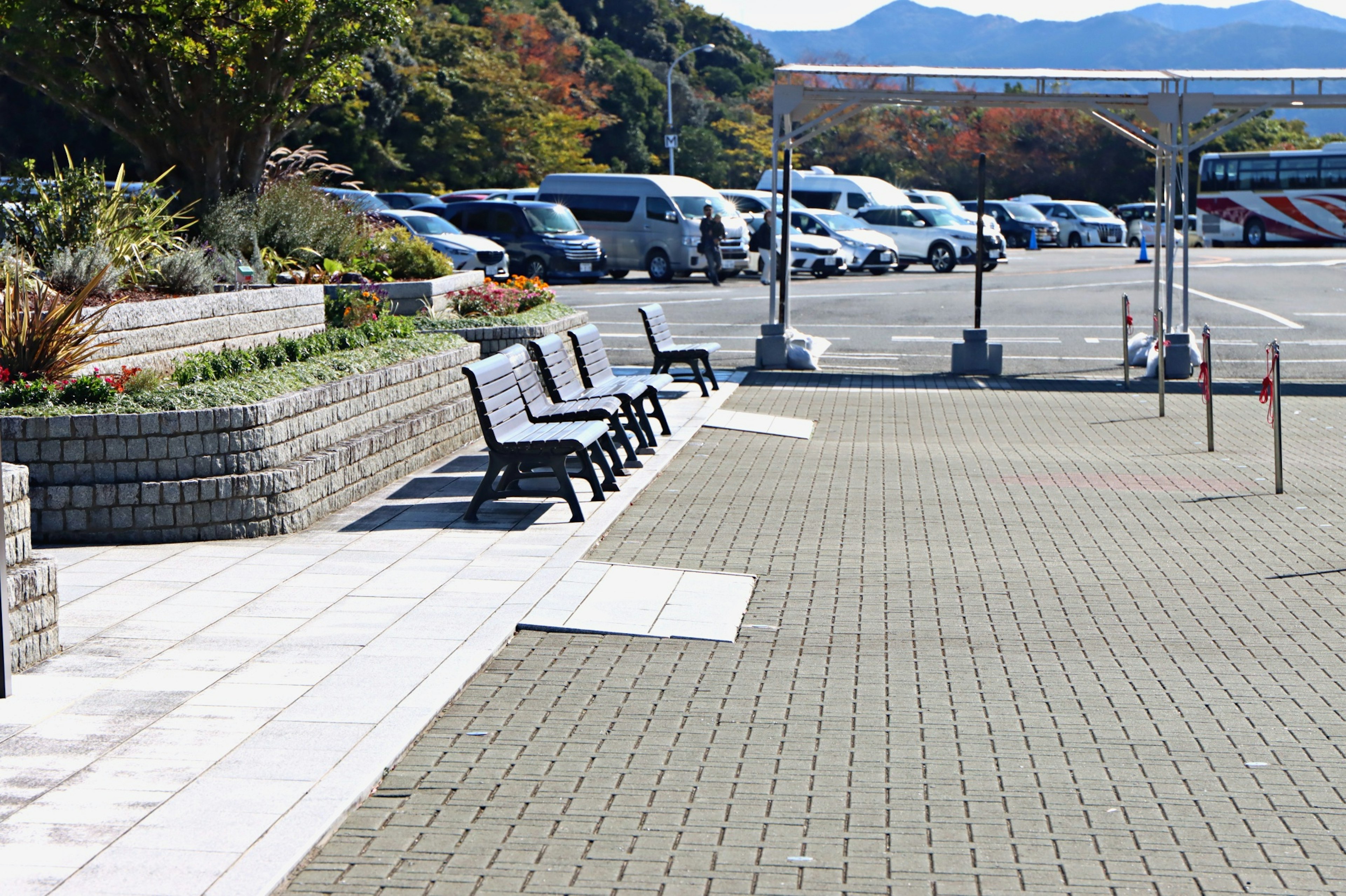 View of a parking area with benches and vehicles surrounded by greenery and distant mountains