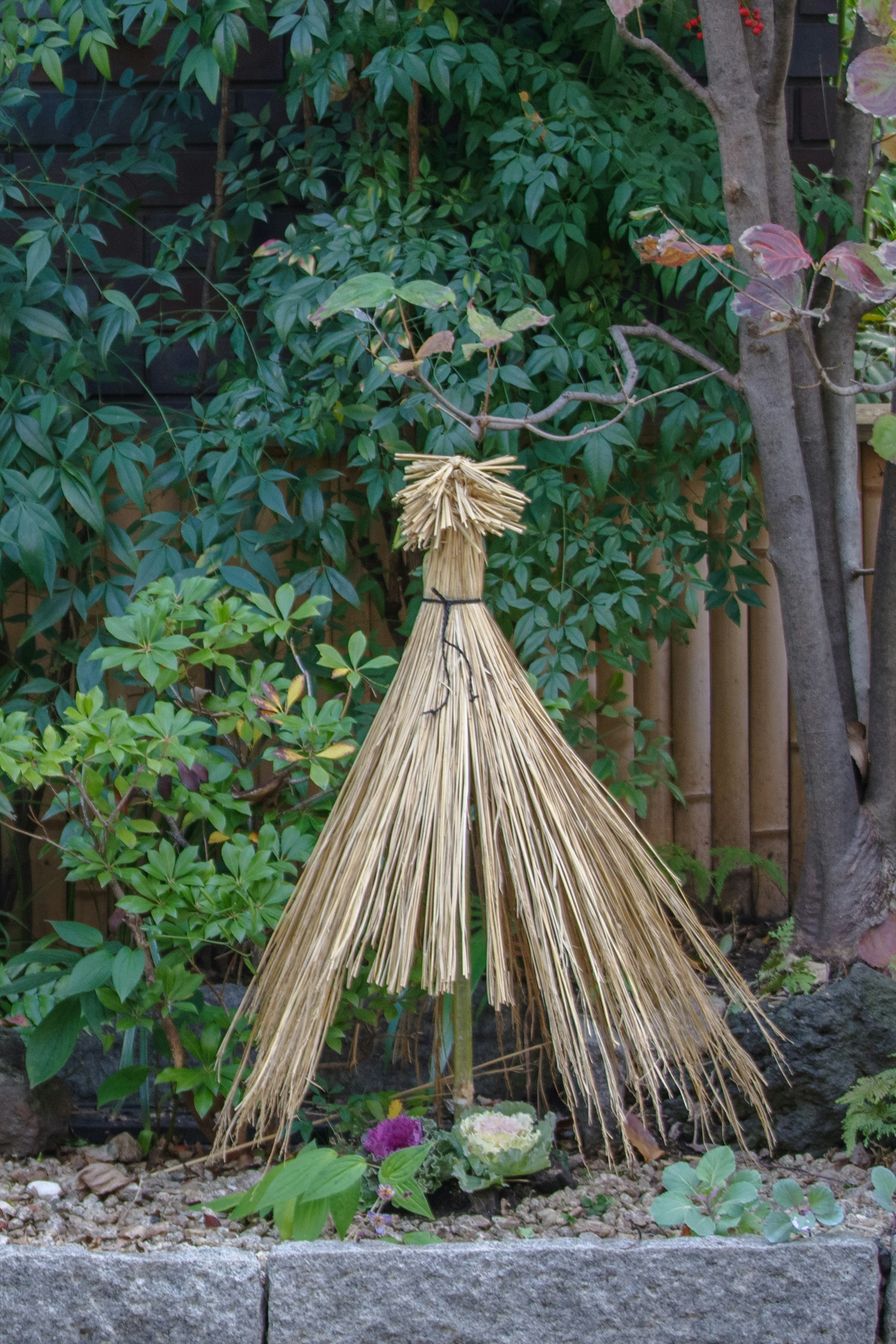 Decorative straw figure standing in a garden surrounded by green plants