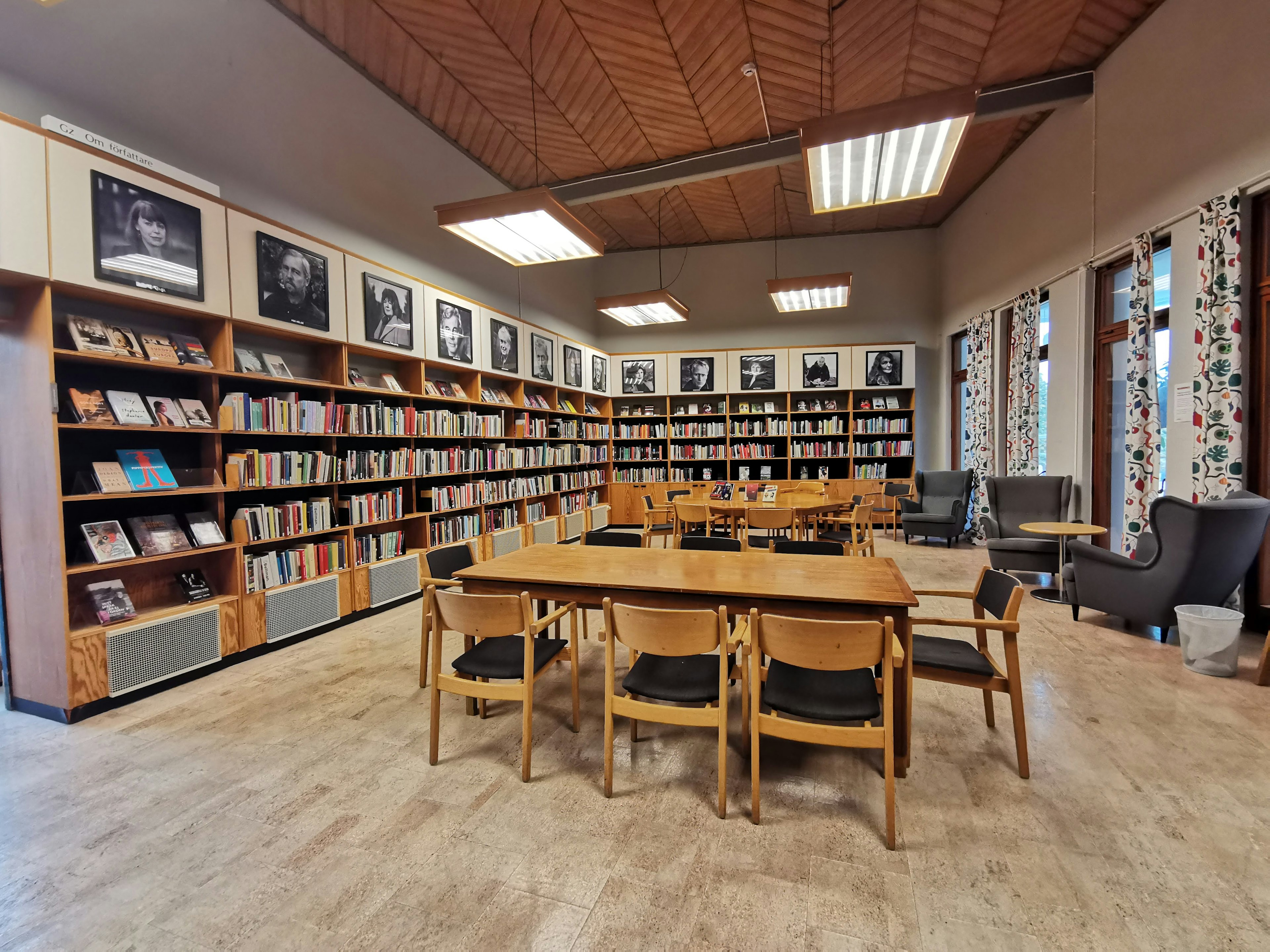 Innenansicht einer ruhigen Bibliothek mit Holztischen und -stühlen Bücherregalen und gerahmten Fotografien an den Wänden