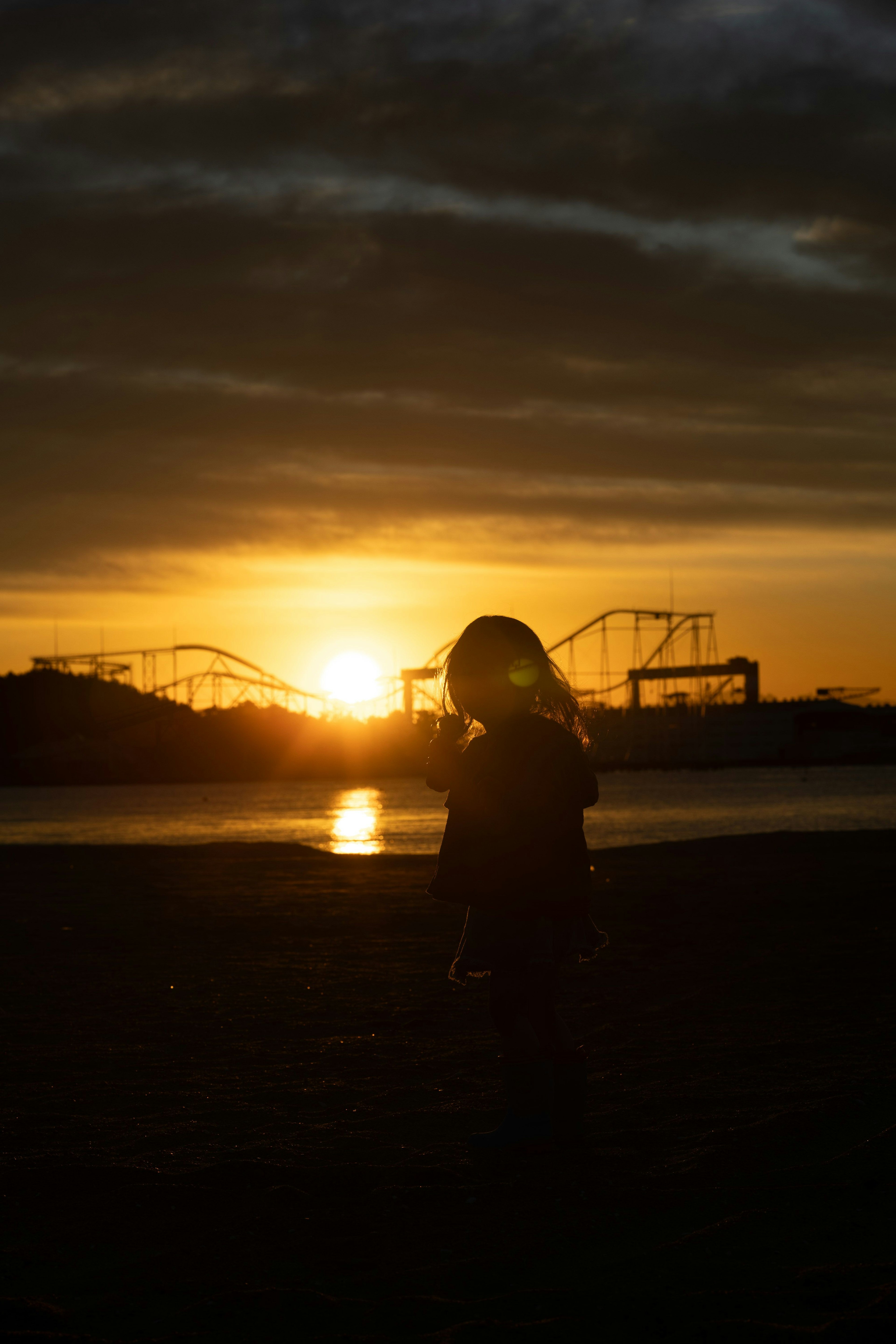 Silhouette d'une femme contre un coucher de soleil avec des montagnes russes d'un parc d'attractions en arrière-plan