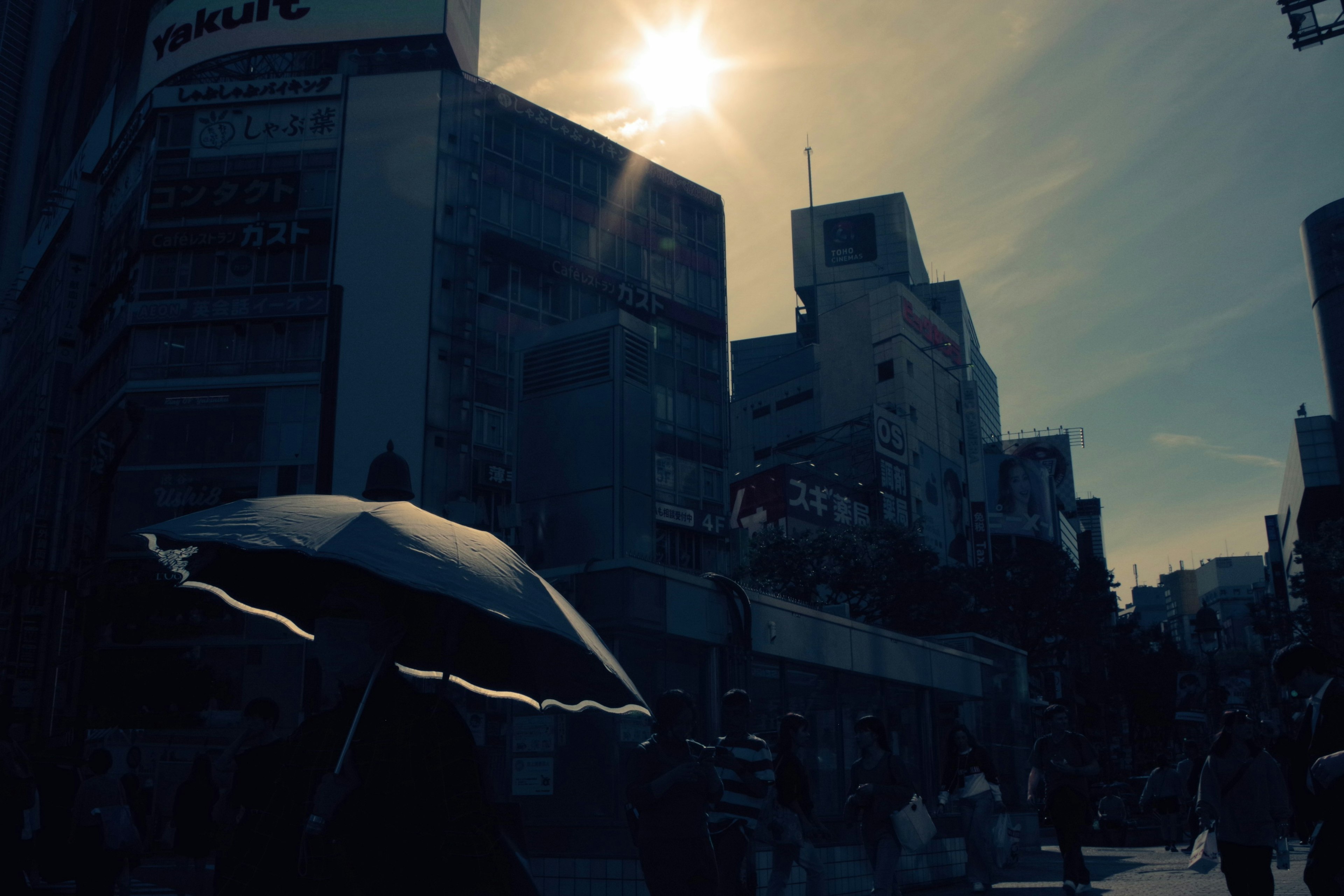 ビルの間を歩く人々と傘を持つシルエット 太陽が輝く街の風景