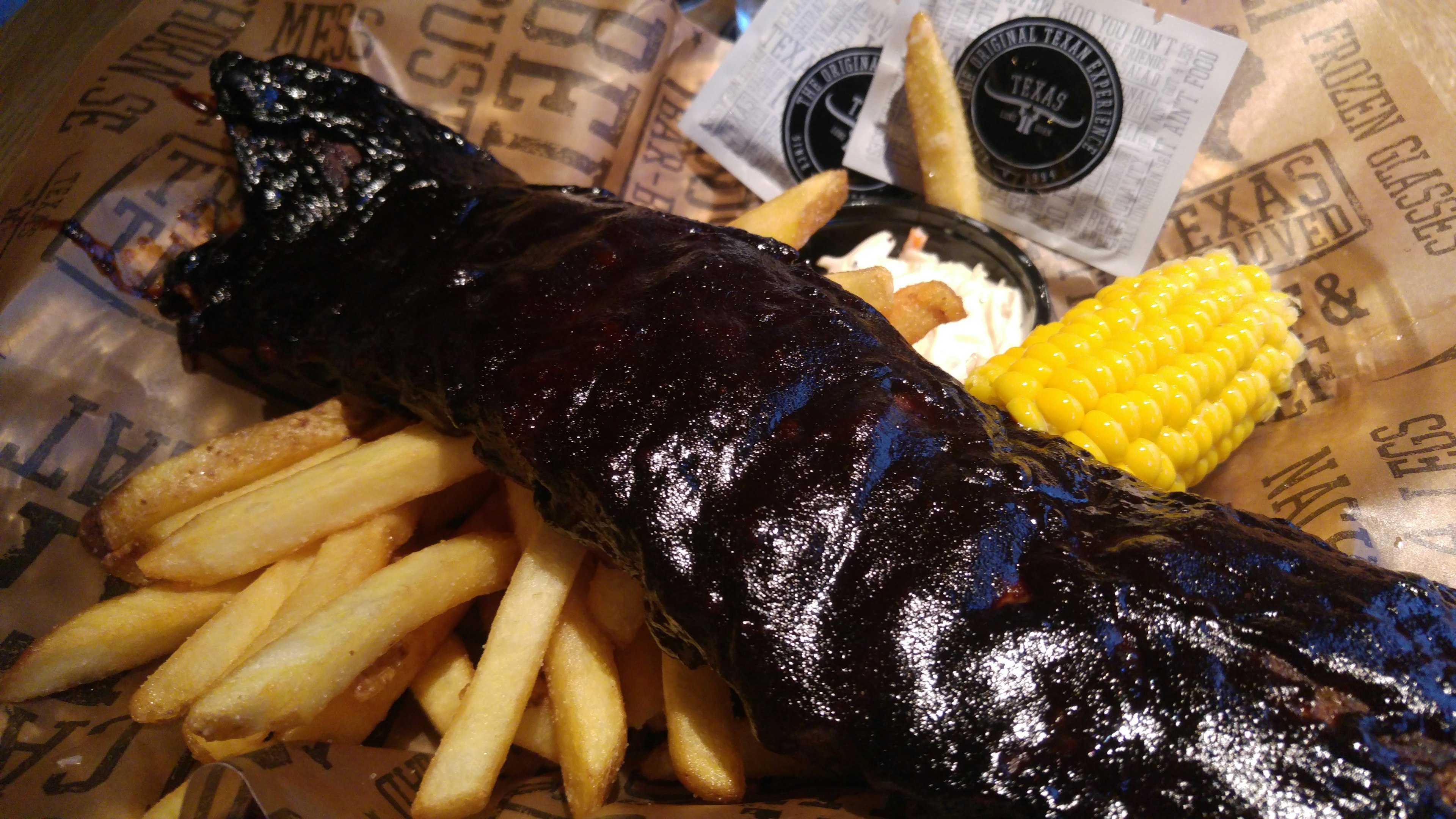 Costillas de cerdo a la barbacoa con salsa oscura servidas con papas fritas y maíz