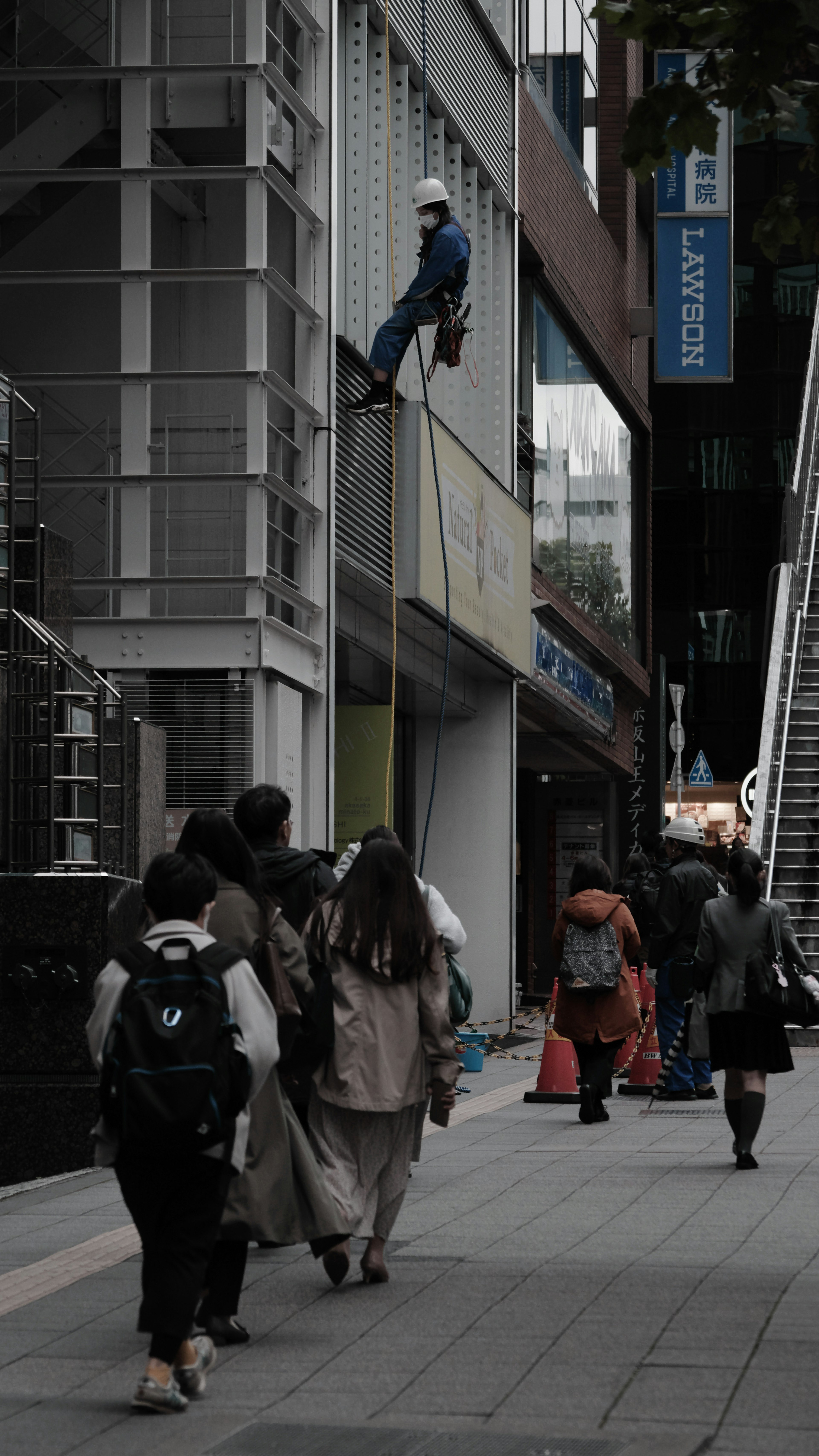 Worker rappelling down a building wall with pedestrians walking below