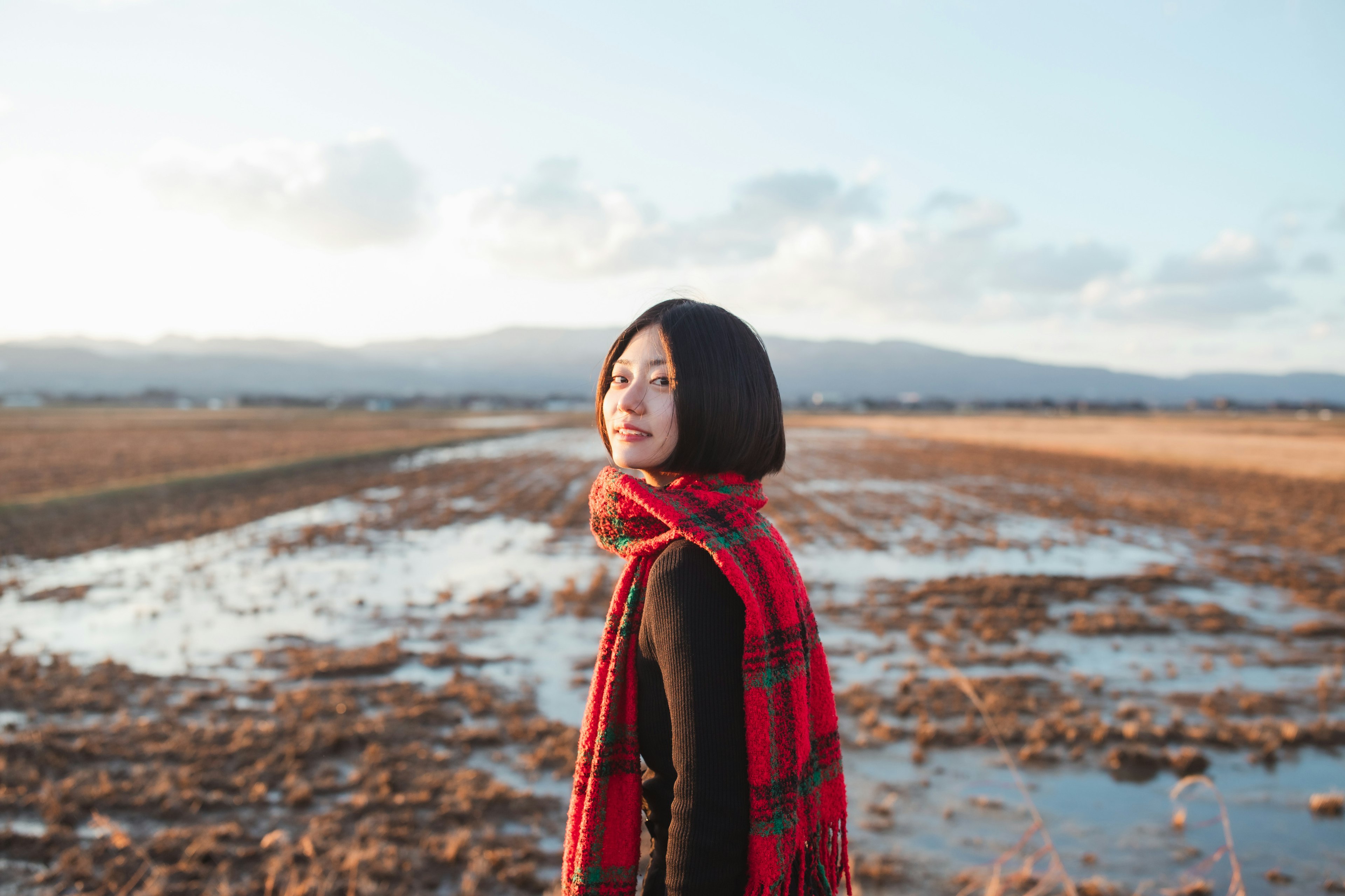 Profile of a woman in a field wearing a red checkered scarf