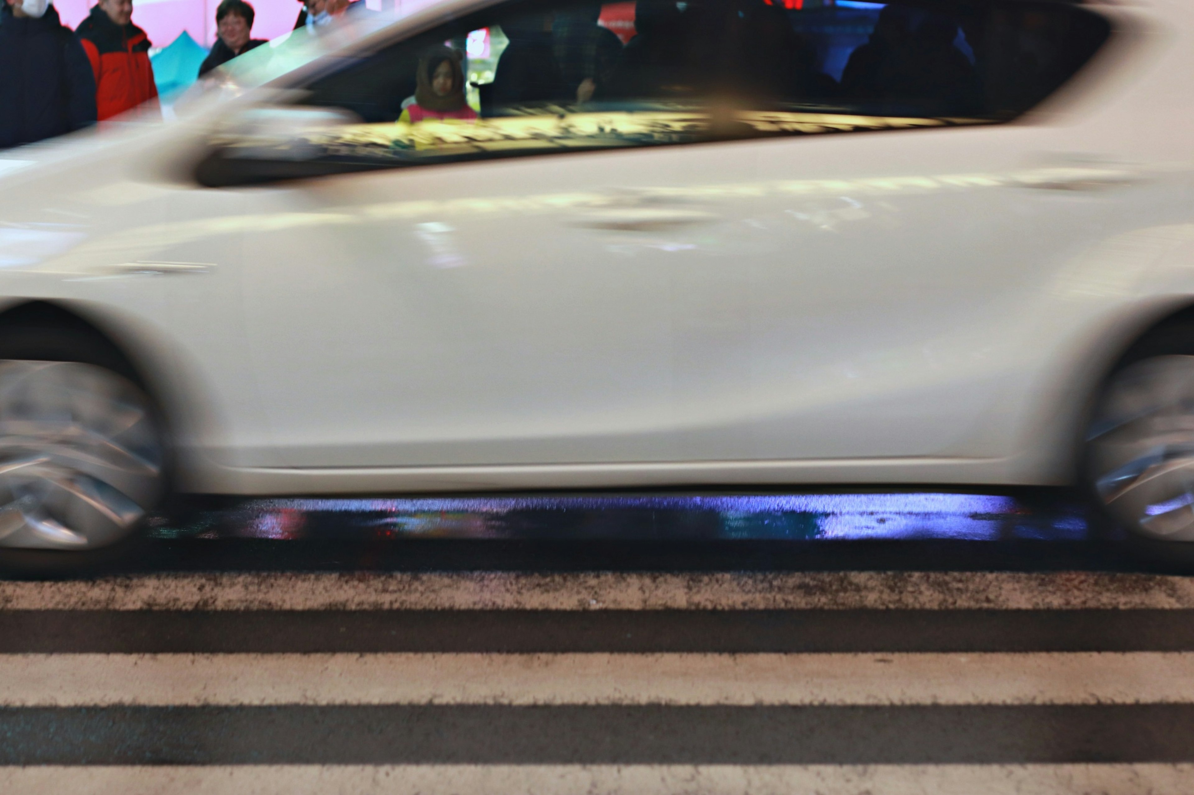 Un coche blanco pasando por un paso de peatones en un entorno urbano nocturno