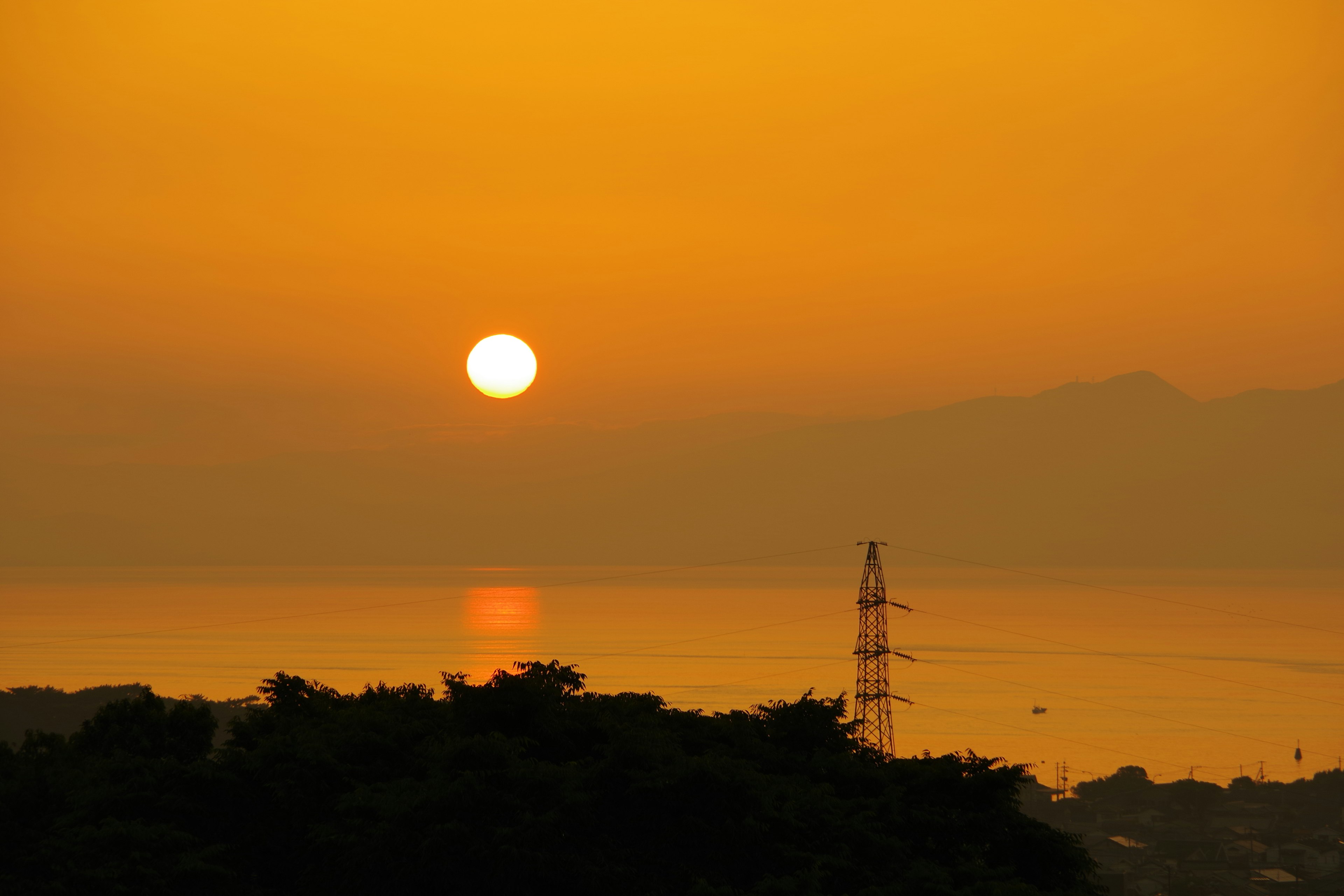 Scenic view of an orange sunset over the sea with a silhouette of hills and a power pole