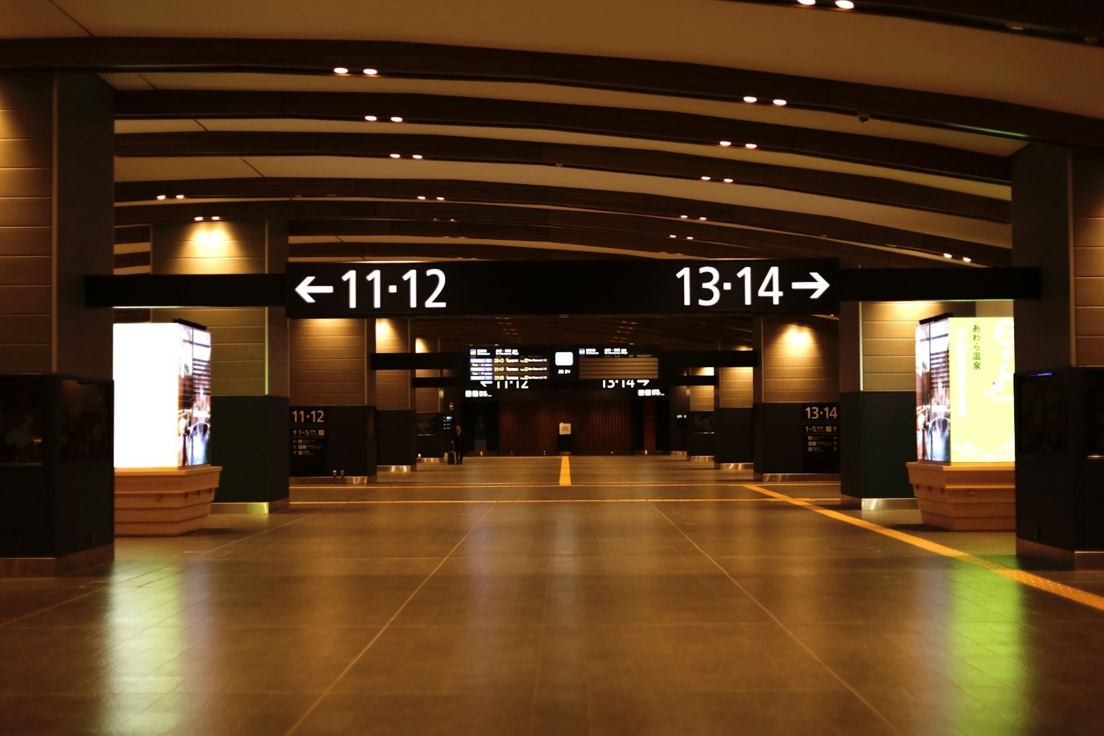 Modern train station interior featuring a spacious corridor with illuminated ceiling numbers 11-12 on the left and 13-14 on the right