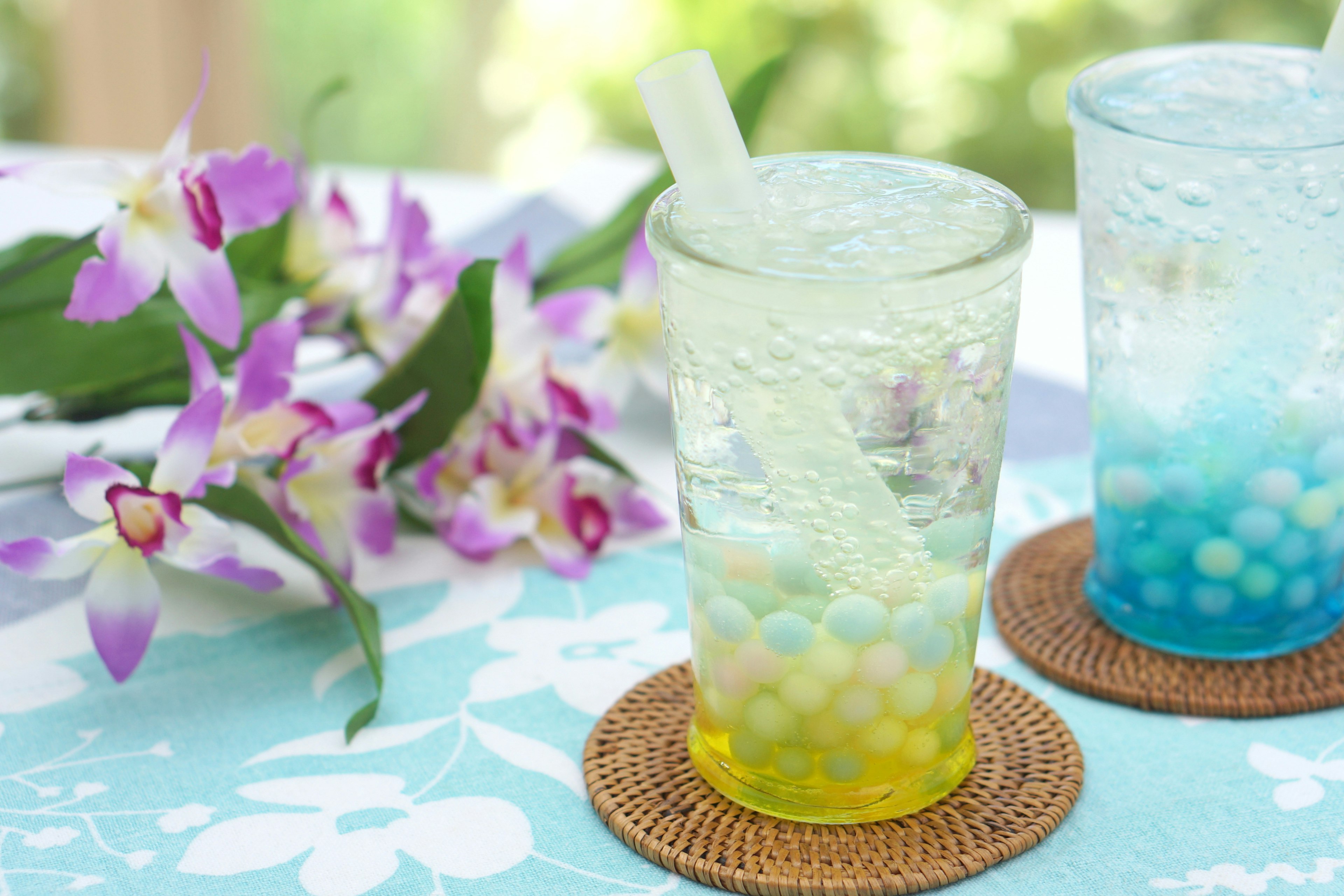 透明なグラスに入ったカラフルな飲み物と紫の花