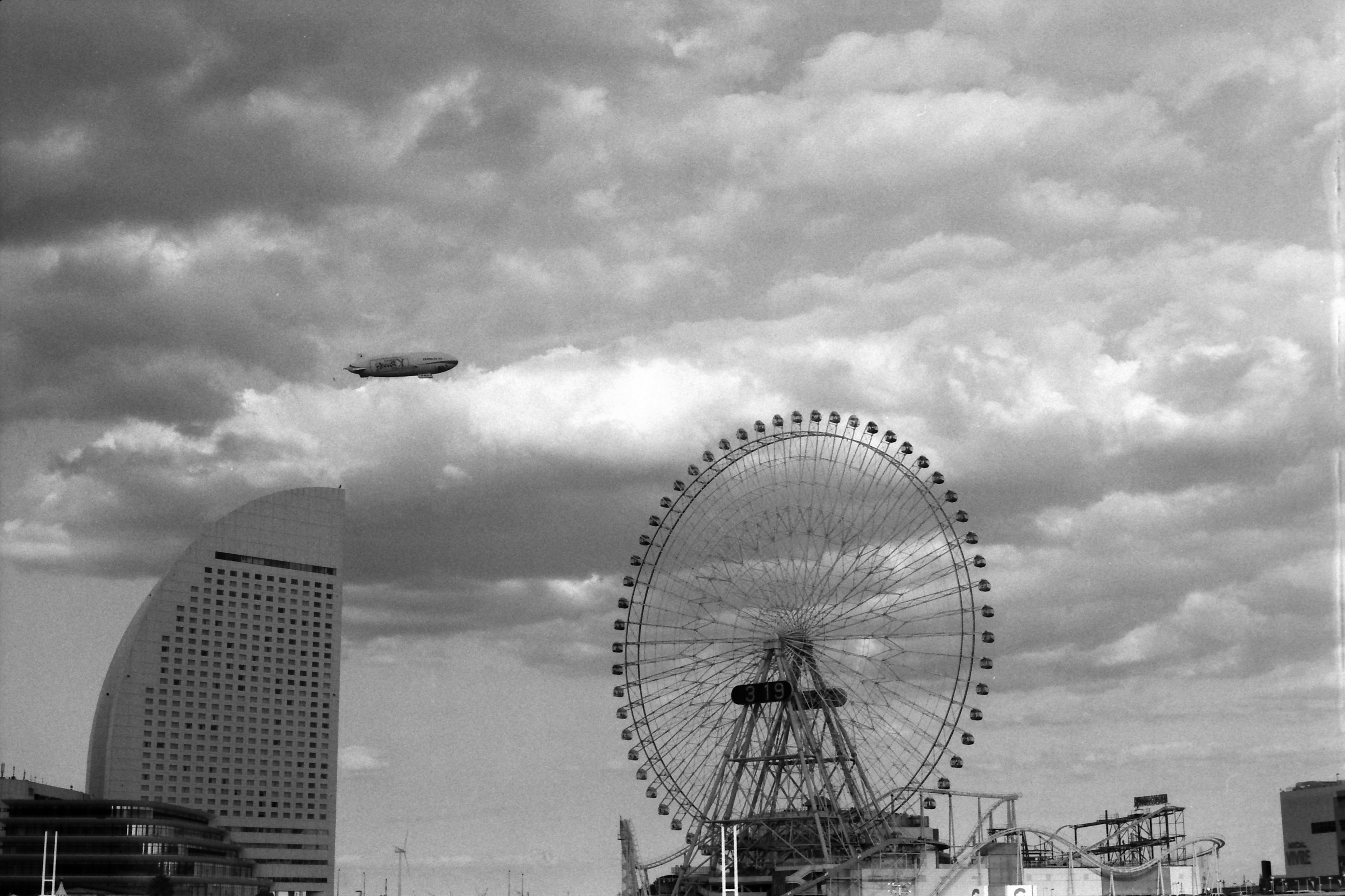 Black and white image of a Ferris wheel against a cloudy sky