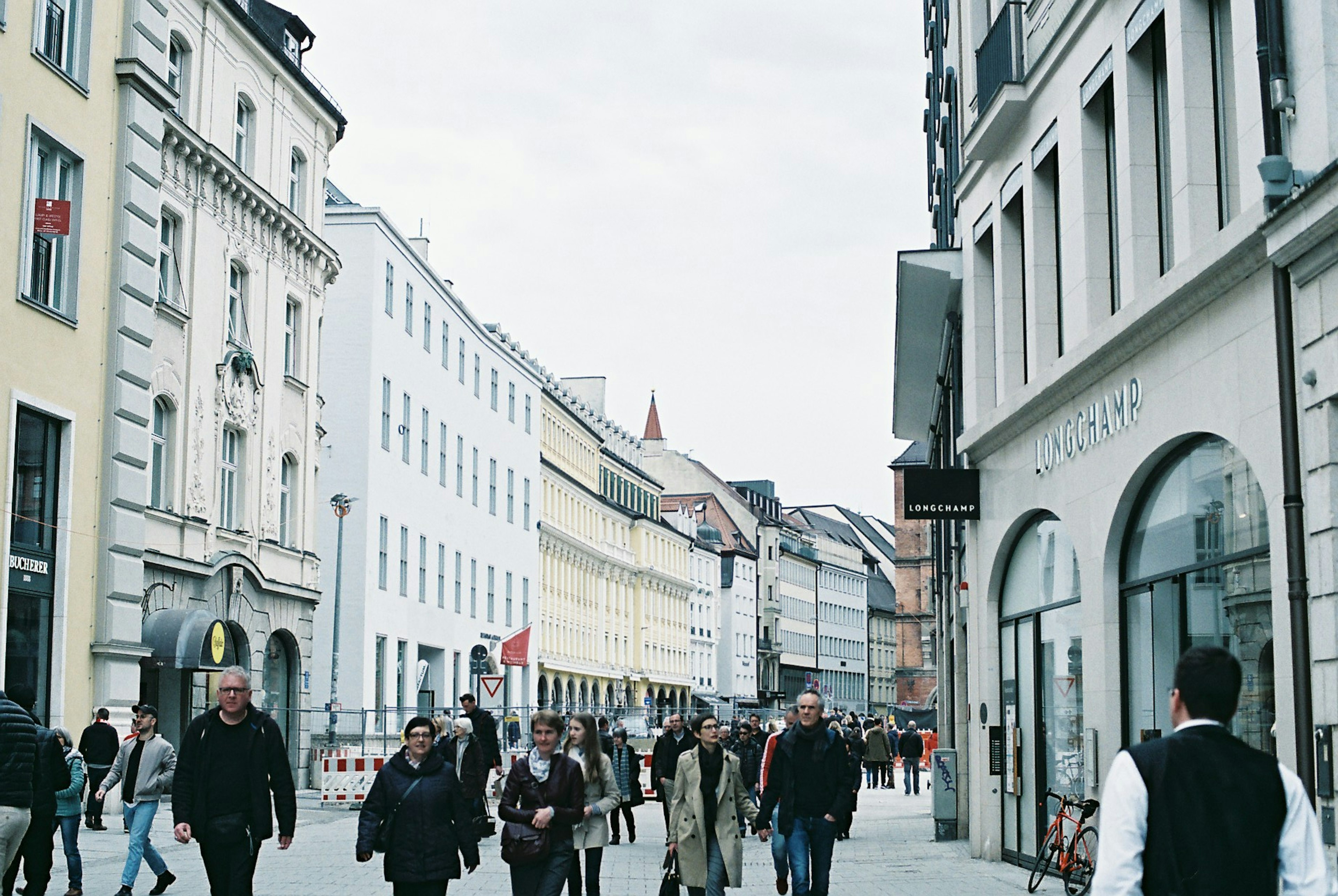 A city street scene with people walking surrounded by white buildings and a gray sky