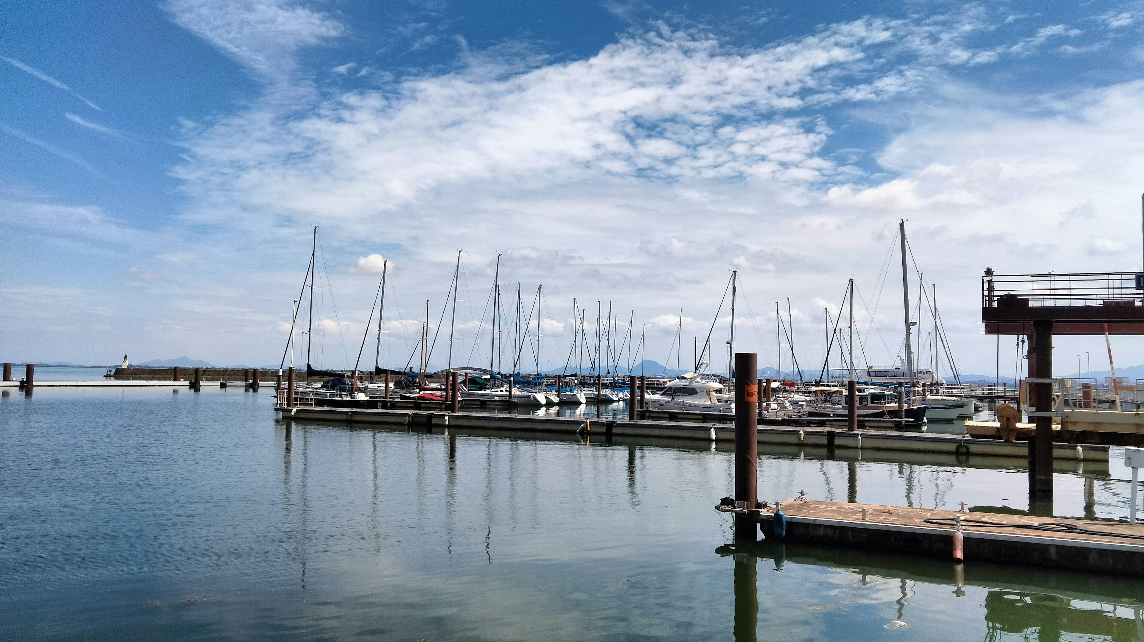 A scenic harbor with moored yachts and boats under a blue sky and clouds