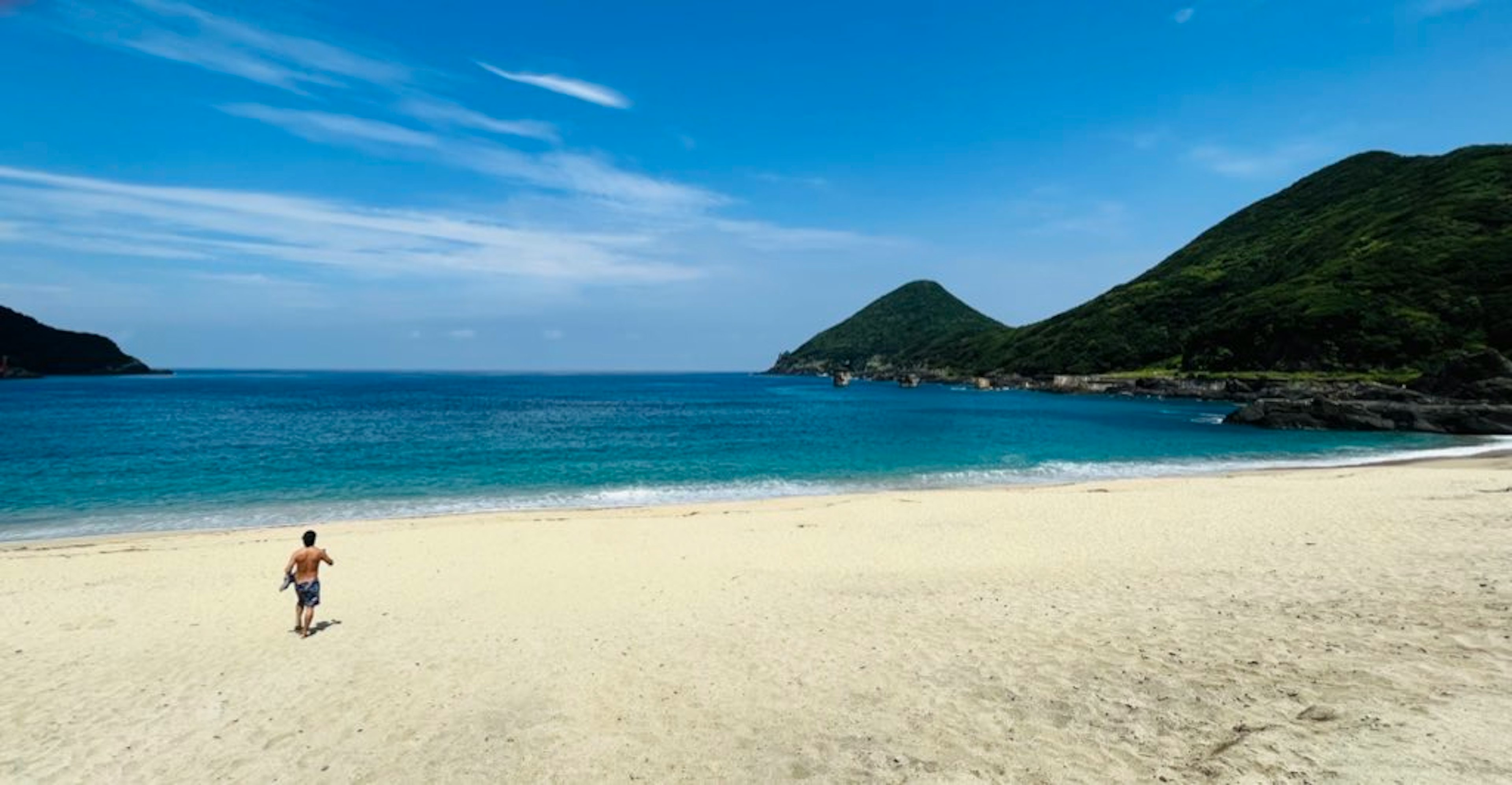 青い海と白い砂浜のビーチを歩く男性